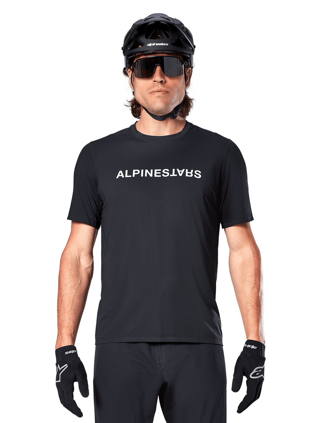Rowerzysta górski w koszulce Alpinestars A-Dura Switch z krótkim rękawem w kolorze czarnym, z białym logo na piersi, stylizacja z czarnym kaskiem, dużymi okularami przeciwsłonecznymi i czarnymi rękawiczkami, profesjonalna odzież rowerowa do jazdy po szlakach