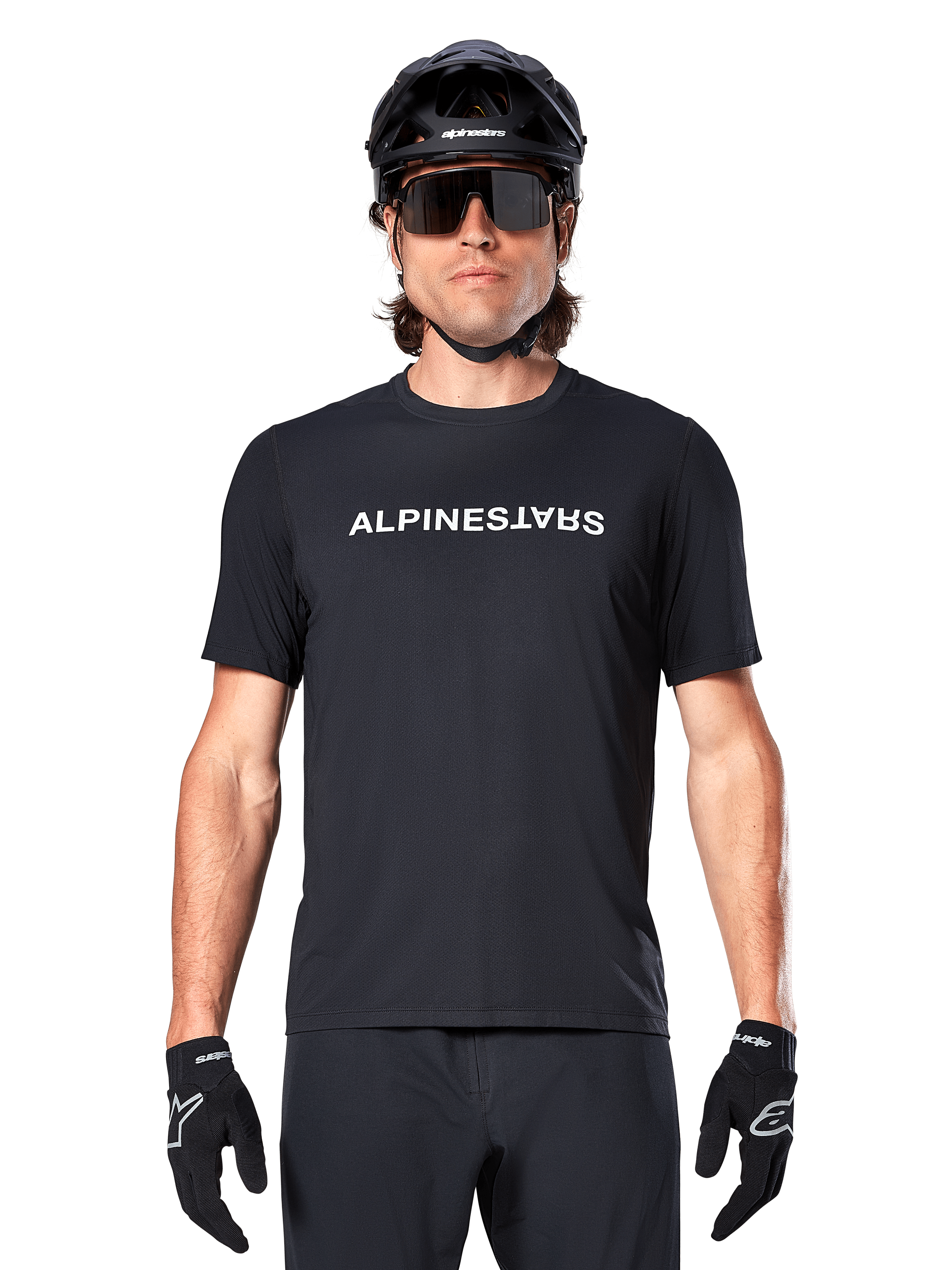 Rowerzysta górski w koszulce Alpinestars A-Dura Switch z krótkim rękawem w kolorze czarnym, z białym logo na piersi, stylizacja z czarnym kaskiem, dużymi okularami przeciwsłonecznymi i czarnymi rękawiczkami, profesjonalna odzież rowerowa do jazdy po szlakach
