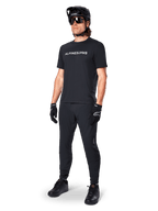 Alpinestars A-Dura Switch Short Sleeve Jersey, czarna, noszona przez modela z dopasowanymi czarnymi spodniami MTB, kaskiem i rękawicami, z białym napisem Alpinestars na piersi, techniczna odzież do kolarstwa górskiego