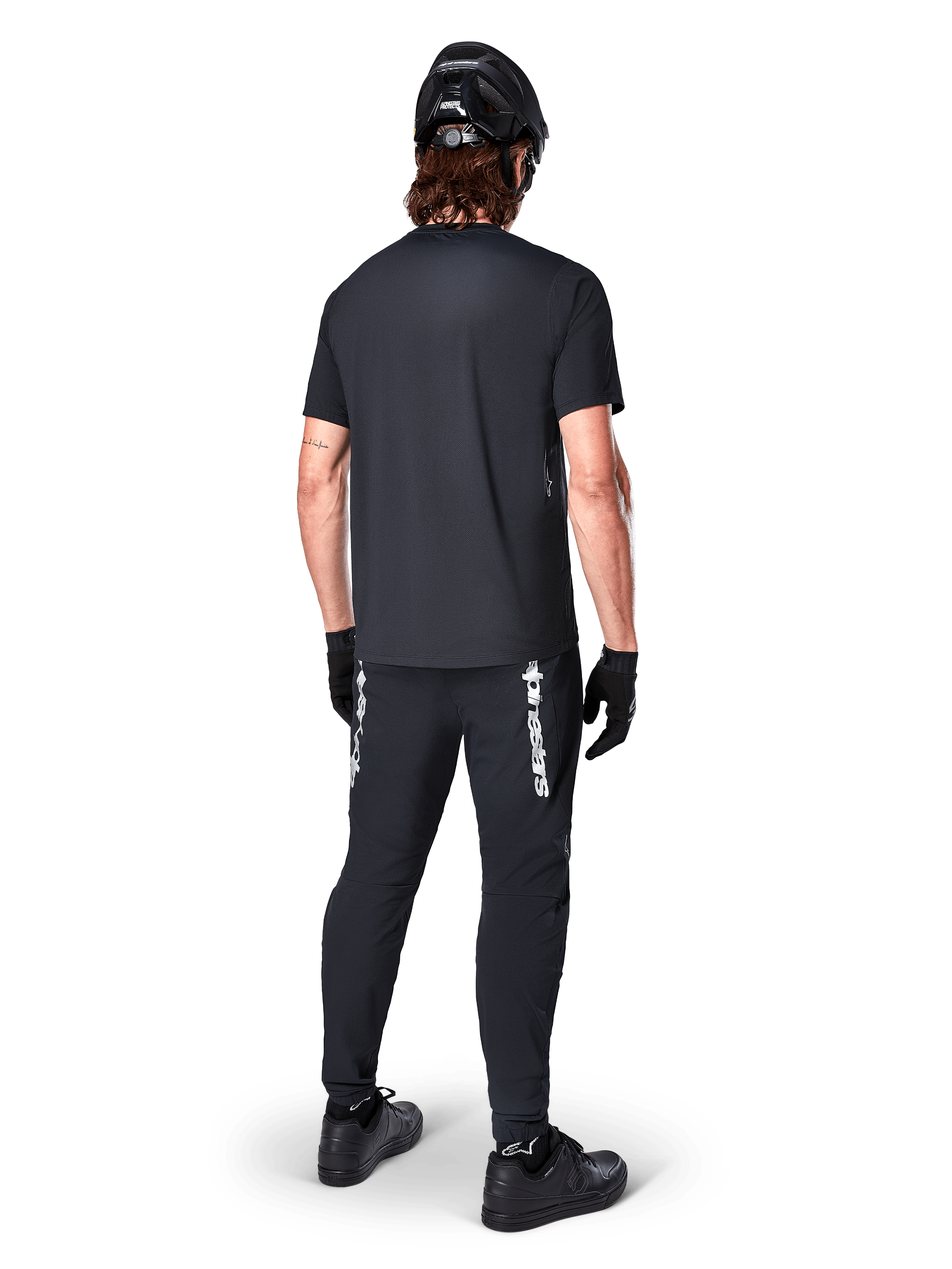 Alpinestars A-Dura Switch Jersey - Short Sleeve, czarna koszulka z krótkim rękawem, widok od tyłu na kolarza w kompletnym stroju MTB, czarne spodnie z białym logotypem, czarny kask i rękawice, techniczna odzież rowerowa do jazdy po szlakach