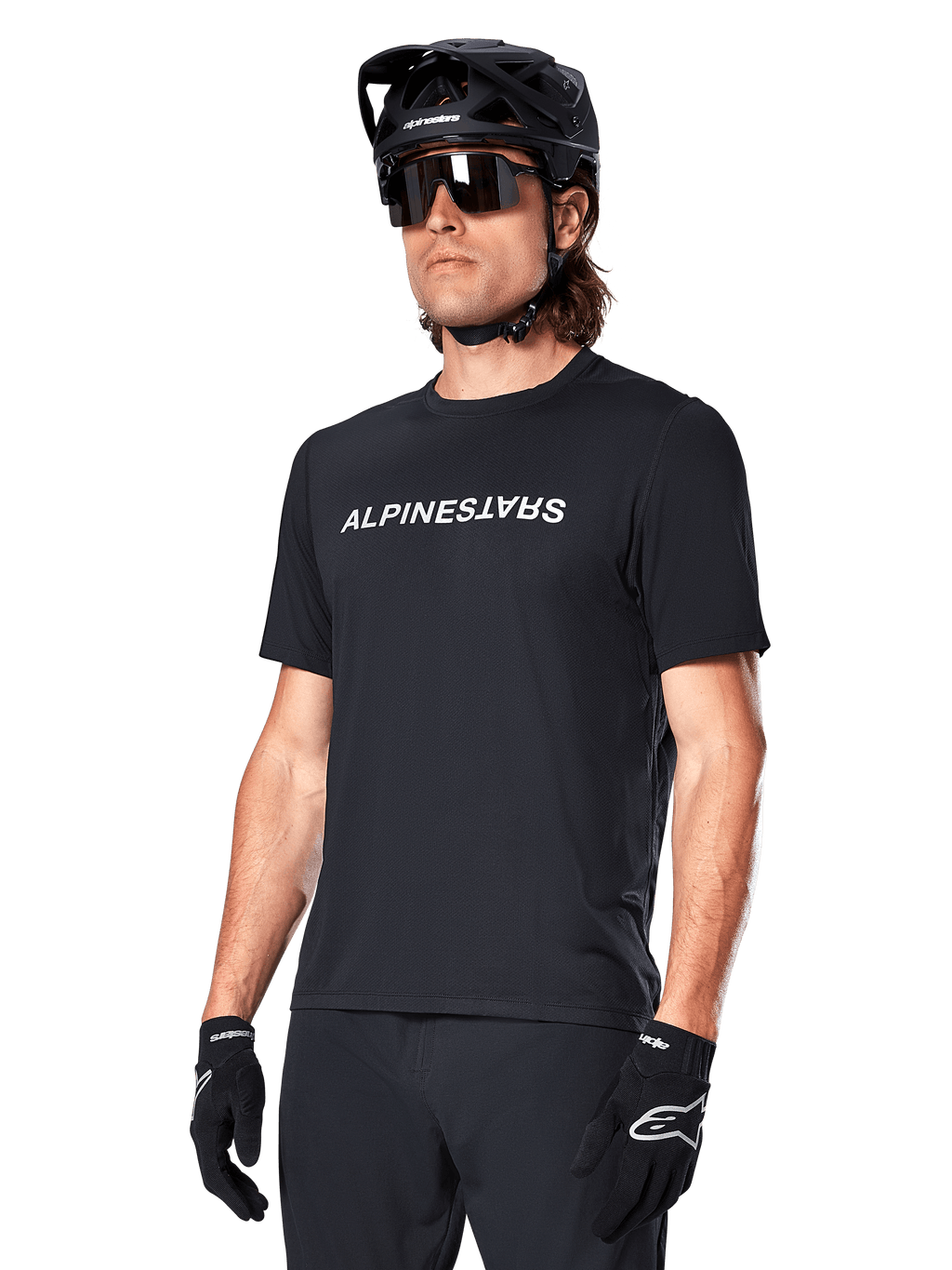 Alpinestars A-Dura Switch Short Sleeve Jersey, czarna koszulka z krótkim rękawem, z białym logotypem na piersi, noszona przez kolarza w czarnym kasku MTB i okularach przeciwsłonecznych, techniczna odzież zaprojektowana do jazdy po szlakach
