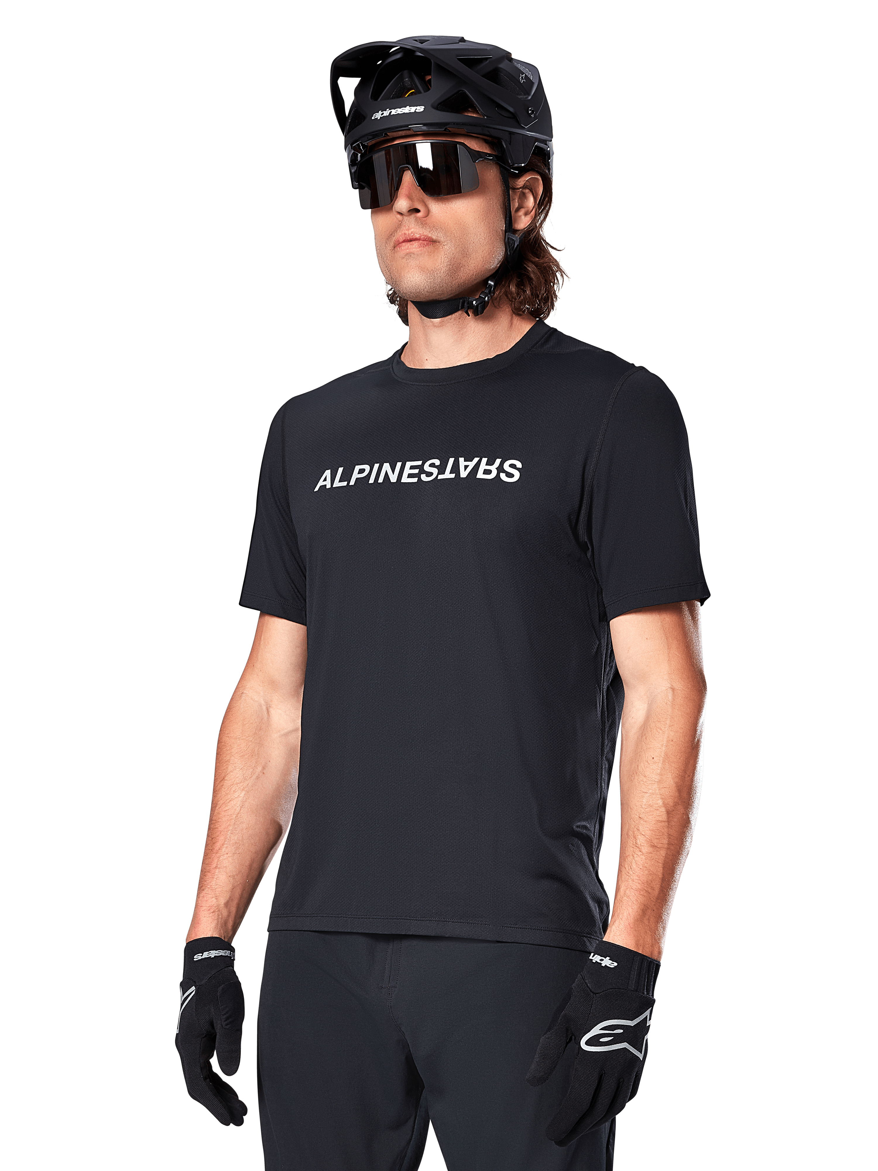 Alpinestars A-Dura Switch Short Sleeve Jersey, czarna koszulka z krótkim rękawem, z białym logotypem na piersi, noszona przez kolarza w czarnym kasku MTB i okularach przeciwsłonecznych, techniczna odzież zaprojektowana do jazdy po szlakach