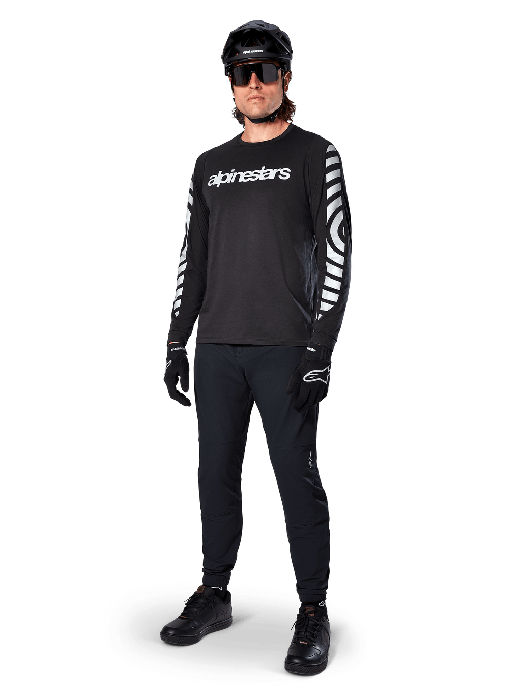Koszulka Alpinestars A-Dura Dri Oscar z długim rękawem, Black Reflective, z wyraźnym białym napisem Alpinestars na klatce piersiowej i odblaskowymi wzorami graficznymi na rękawach, noszona z czarnymi spodniami MTB, kaskiem i rękawicami, techniczna odzież MTB