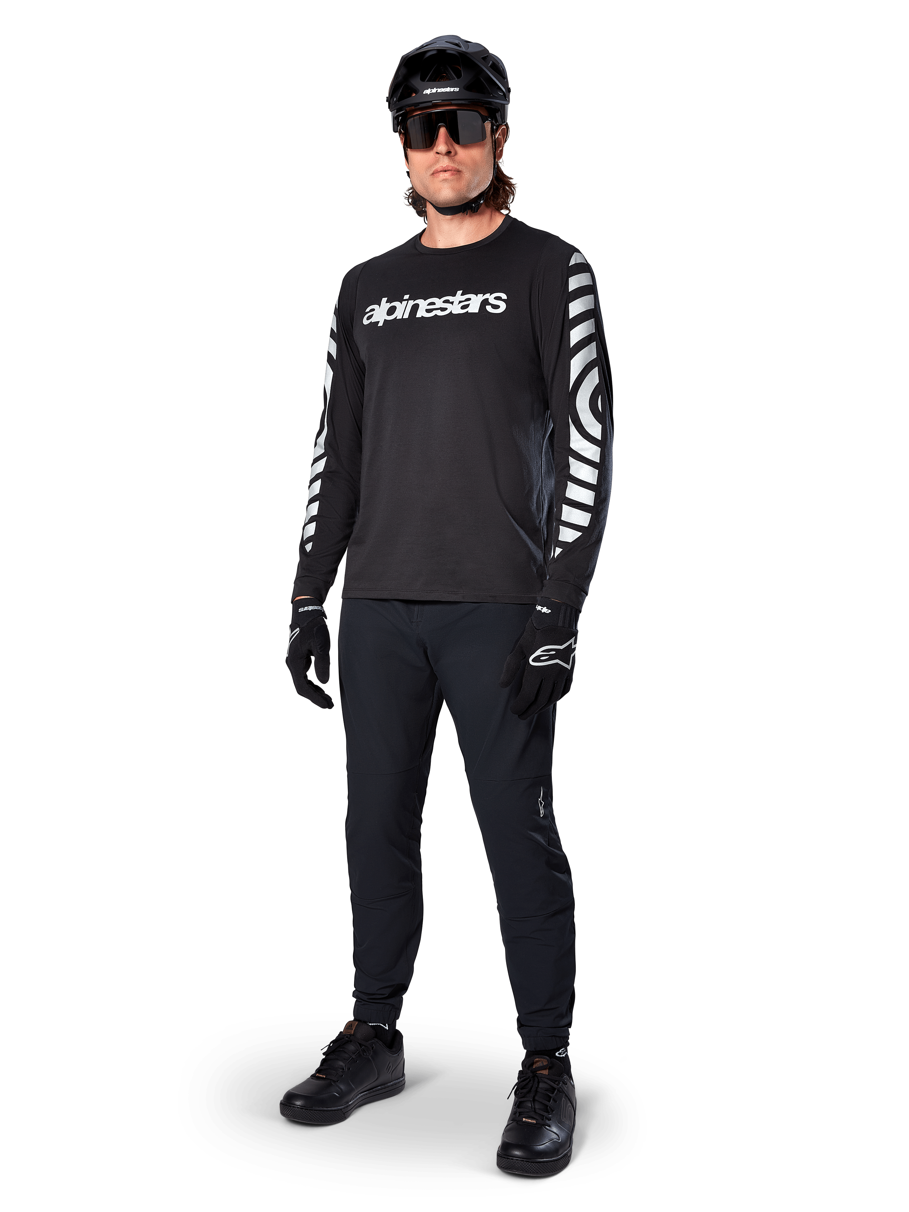 Koszulka Alpinestars A-Dura Dri Oscar z długim rękawem, Black Reflective, z wyraźnym białym napisem Alpinestars na klatce piersiowej i odblaskowymi wzorami graficznymi na rękawach, noszona z czarnymi spodniami MTB, kaskiem i rękawicami, techniczna odzież MTB