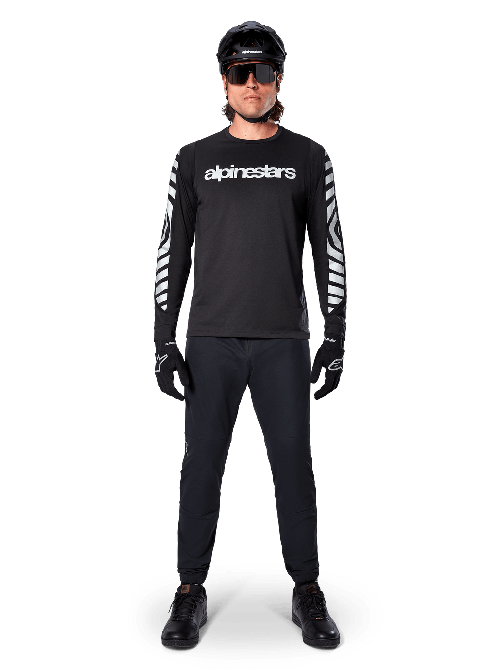 Koszulka Alpinestars A-Dura Dri Oscar Long Sleeve, kolor Black Reflective, noszona z czarnym kaskiem i okularami przeciwsłonecznymi, białe logo na piersi i odblaskowe wzory graficzne na rękawach, odzież MTB do jazdy terenowej