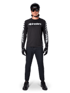 Koszulka Alpinestars A-Dura Dri Oscar Long Sleeve, kolor Black Reflective, noszona z czarnym kaskiem i okularami przeciwsłonecznymi, białe logo na piersi i odblaskowe wzory graficzne na rękawach, odzież MTB do jazdy terenowej