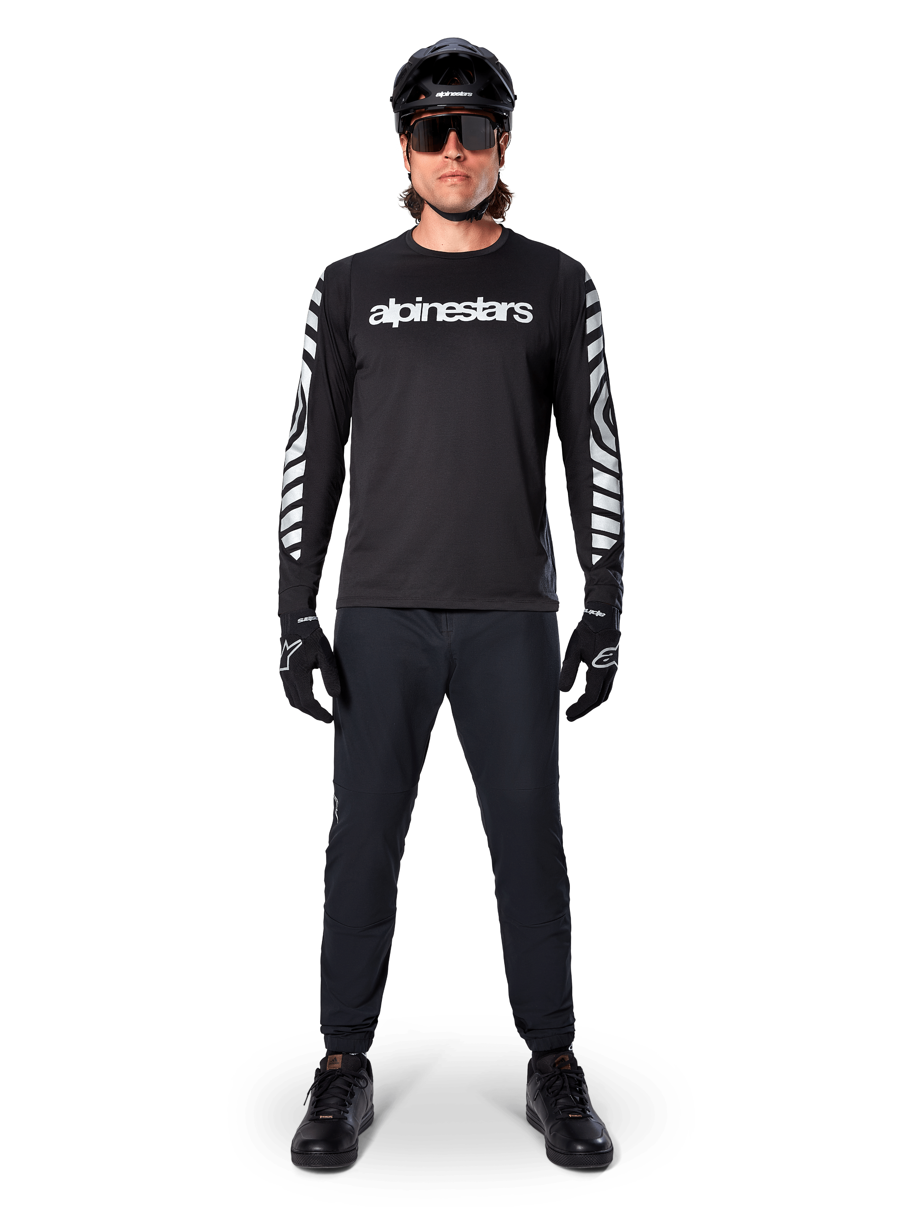 Koszulka Alpinestars A-Dura Dri Oscar Long Sleeve, kolor Black Reflective, noszona z czarnym kaskiem i okularami przeciwsłonecznymi, białe logo na piersi i odblaskowe wzory graficzne na rękawach, odzież MTB do jazdy terenowej