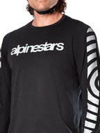 Alpinestars A-Dura Dri Oscar Long Sleeve Jersey, Black Reflective, koszulka rowerowa z długim rękawem, widok z bliska na białe logo Alpinestars na klatce piersiowej i odblaskowe koliste grafiki na rękawach, techniczna odzież do jazdy MTB