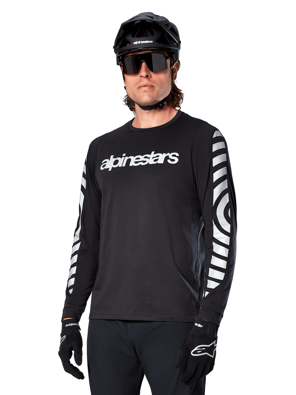 Koszulka z długim rękawem Alpinestars A-Dura Dri Oscar, koszulka rowerowa MTB, czarna odblaskowa, z białym napisem na klatce piersiowej i wyraźnymi odblaskowymi grafikami na rękawach, noszona z czarnym kaskiem i okularami przeciwsłonecznymi, techniczna odzież odprowadzająca wilgoć do jazdy terenowej na rowerze górskim