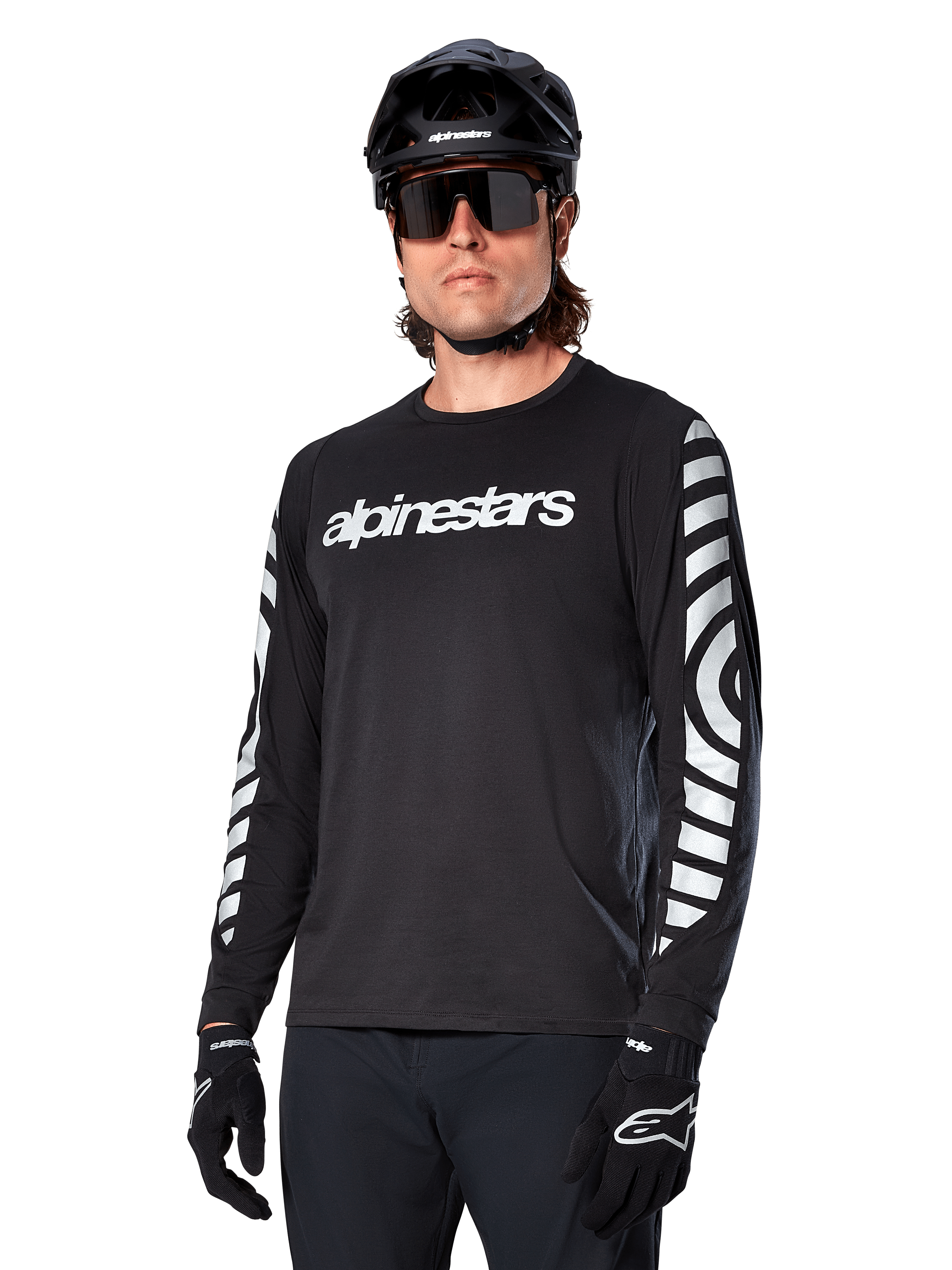 Alpinestars A-Dura Dri Oscar Long Sleeve Jersey, MTB Cycling Jersey, Black Reflective, featuring a white chest wordmark and bold reflective circular graphics on the sleeves, worn with a black helmet and sunglasses, technical moisture-wicking apparel for off-road mountain biking