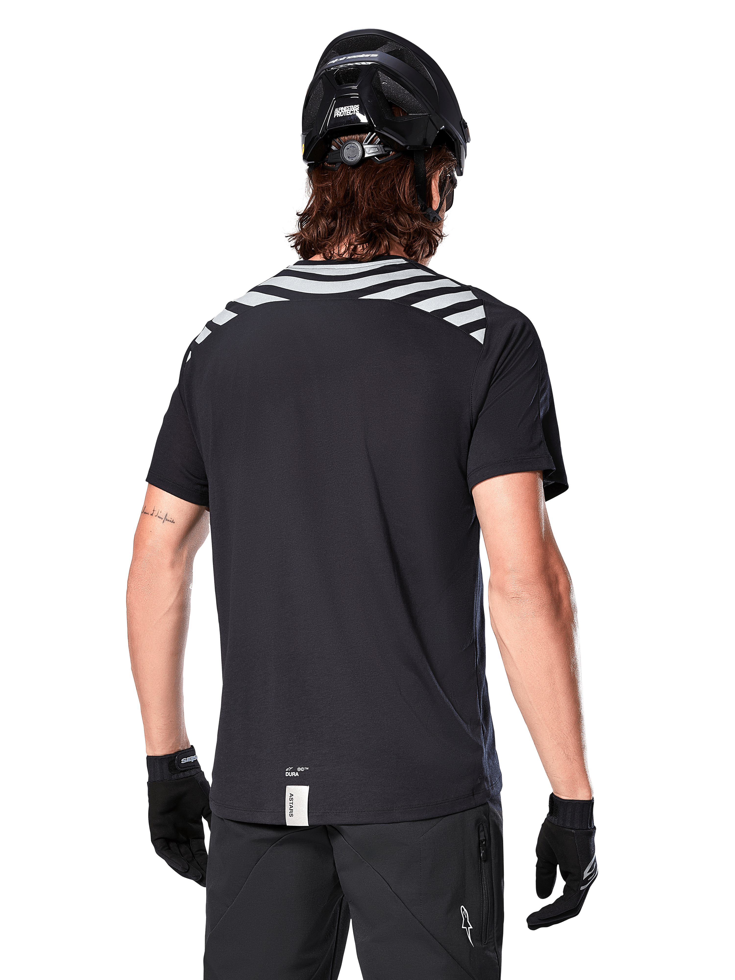 Alpinestars A-Dura Dri Oscar Jersey, koszulka MTB z krótkim rękawem, Black Reflective, widok z tyłu na modelu w kasku rowerowym i rękawiczkach, z odblaskowymi szarymi pasami na ramionach i przedłużonym tyłem, techniczny materiał odprowadzający wilgoć do jazdy na rowerze górskim