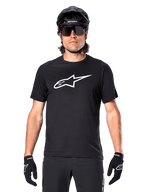 Alpinestars A-Dura Dri Oscar Jersey - Short Sleeve, Black Reflective, koszulka z krótkim rękawem noszona z czarnym kaskiem MTB, okularami przeciwsłonecznymi i rękawiczkami, z wyraźnym białym logo na piersi, odzież wyczynowa do kolarstwa górskiego
