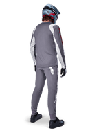 Alpinestars A-Supra Astar Jersey, koszulka MTB z długim rękawem, ciemnoszara z białymi akcentami na rękawach i czerwonym logo, widok od tyłu na rowerzystę w pasujących szarych spodniach i niebieskim kasku full-face, techniczna odzież rowerowa