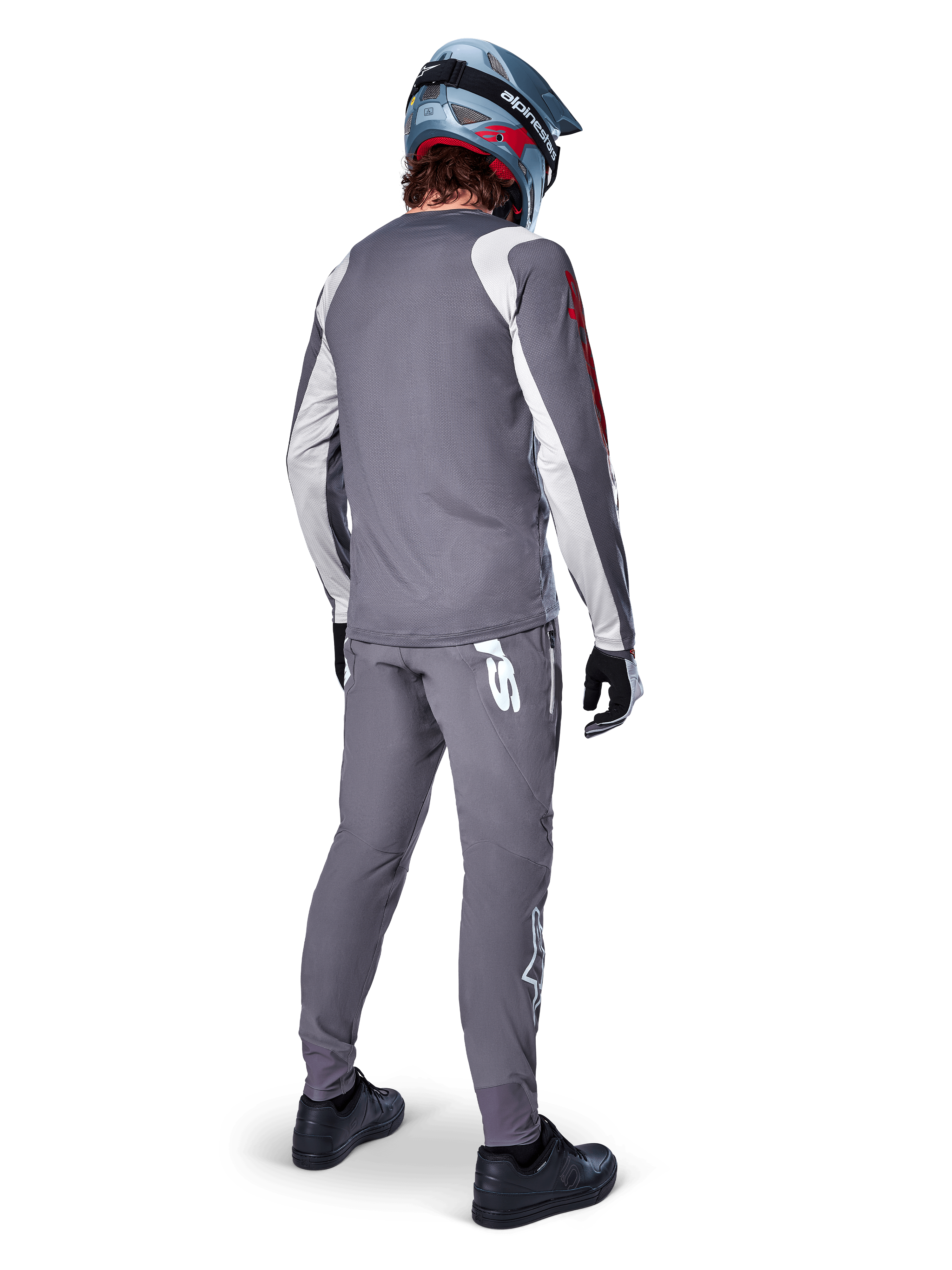 Alpinestars A-Supra Astar Jersey, koszulka MTB z długim rękawem, ciemnoszara z białymi akcentami na rękawach i czerwonym logo, widok od tyłu na rowerzystę w pasujących szarych spodniach i niebieskim kasku full-face, techniczna odzież rowerowa
