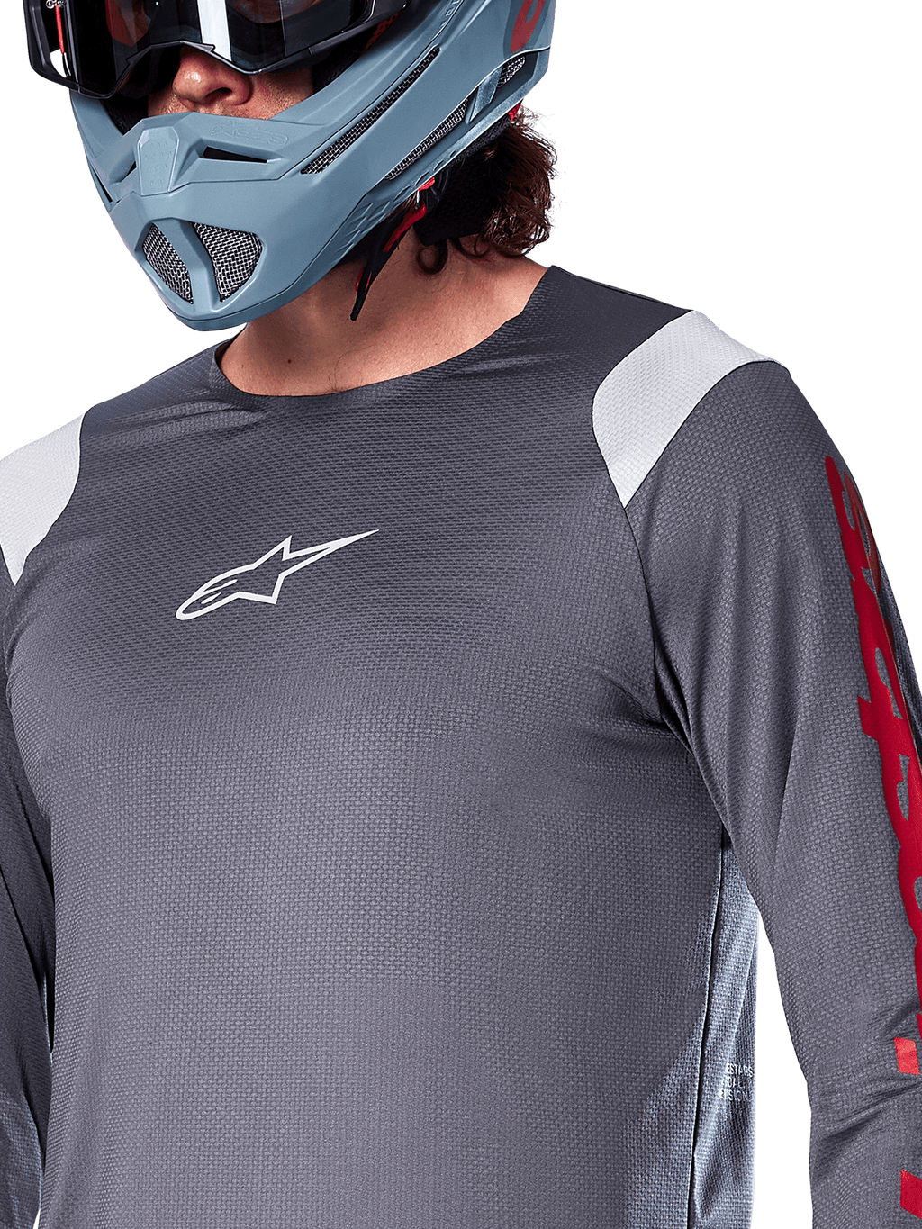 Alpinestars A-Supra Astar Long Sleeve Jersey, koszulka z długim rękawem, ciemnoszara z białymi panelami na ramionach i czerwonymi grafikami na rękawach, noszona z jasnym niebiesko-szarym kaskiem full-face, profesjonalna odzież do kolarstwa górskiego