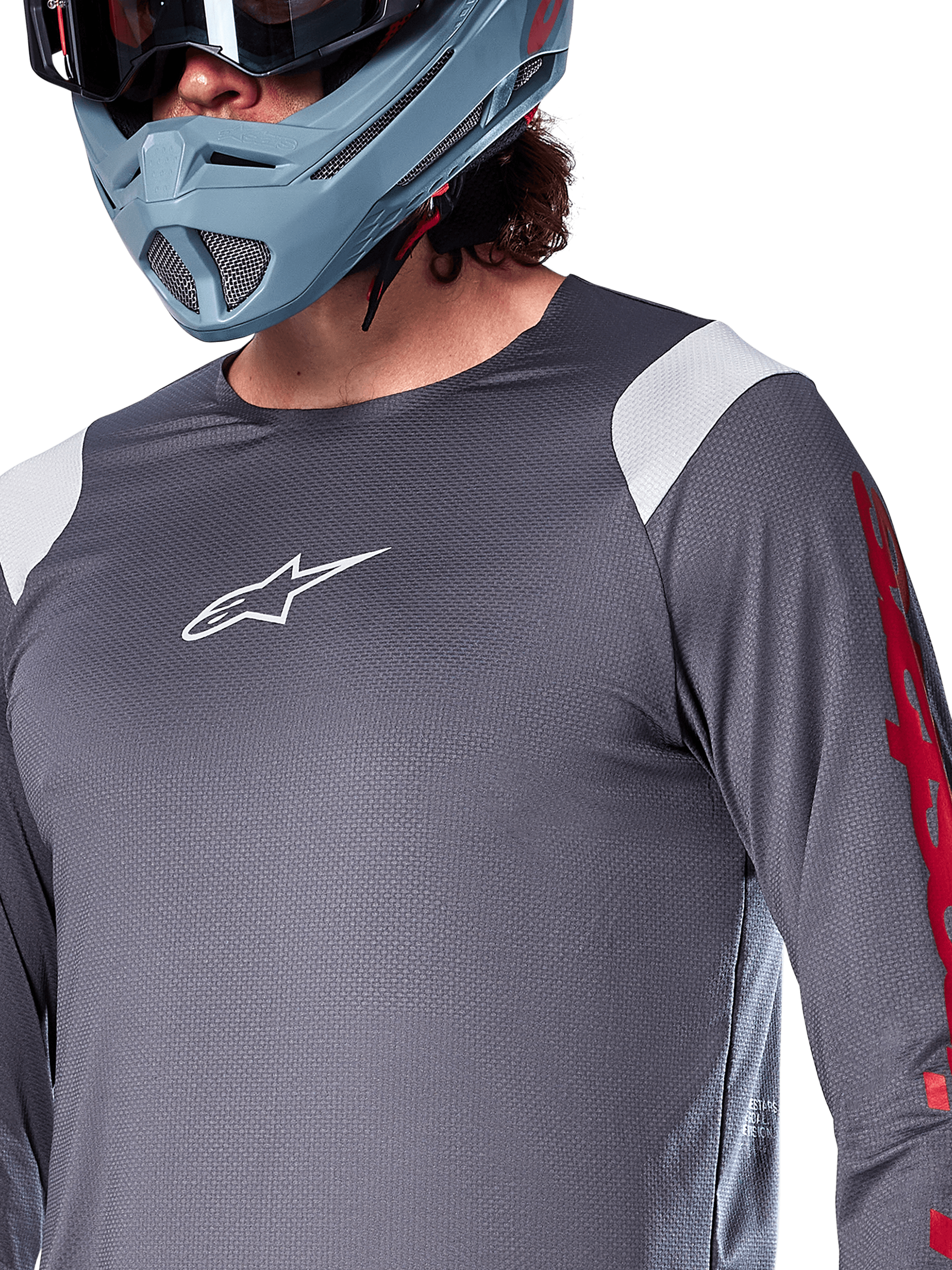Alpinestars A-Supra Astar Long Sleeve Jersey, koszulka z długim rękawem, ciemnoszara z białymi panelami na ramionach i czerwonymi grafikami na rękawach, noszona z jasnym niebiesko-szarym kaskiem full-face, profesjonalna odzież do kolarstwa górskiego