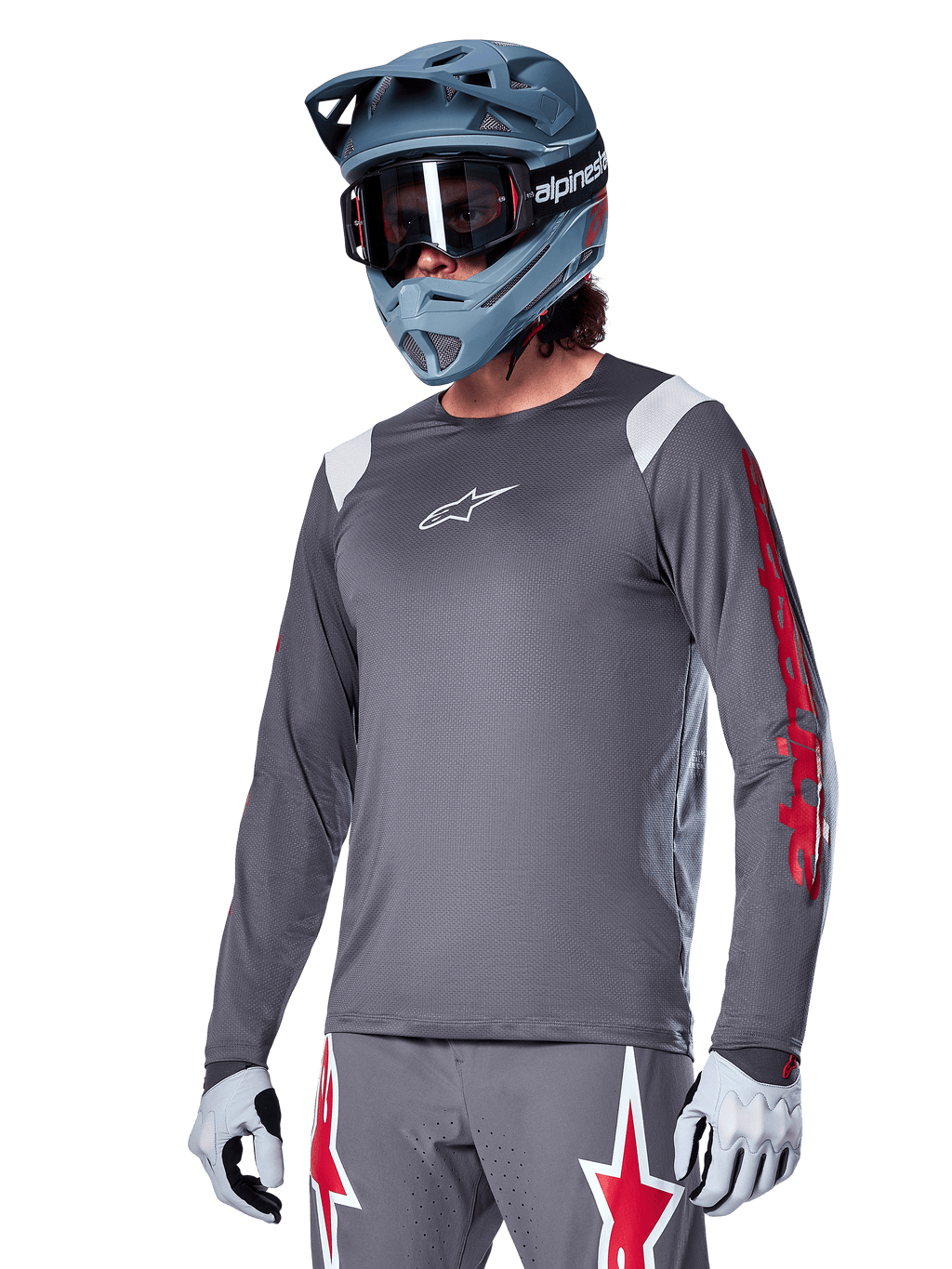 Alpinestars A-Supra Astar Jersey z długim rękawem, koszulka rowerowa MTB, ciemnoszara z czerwonymi i białymi akcentami, sportowy krój, noszona z pasującymi szarymi spodniami z grafiką czerwonych i białych gwiazd, kompletny strój do kolarstwa terenowego z kaskiem full-face i rękawicami