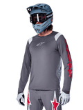 Alpinestars A-Supra Astar Jersey z długim rękawem, koszulka rowerowa MTB, ciemnoszara z czerwonymi i białymi akcentami, sportowy krój, noszona z pasującymi szarymi spodniami z grafiką czerwonych i białych gwiazd, kompletny strój do kolarstwa terenowego z kaskiem full-face i rękawicami