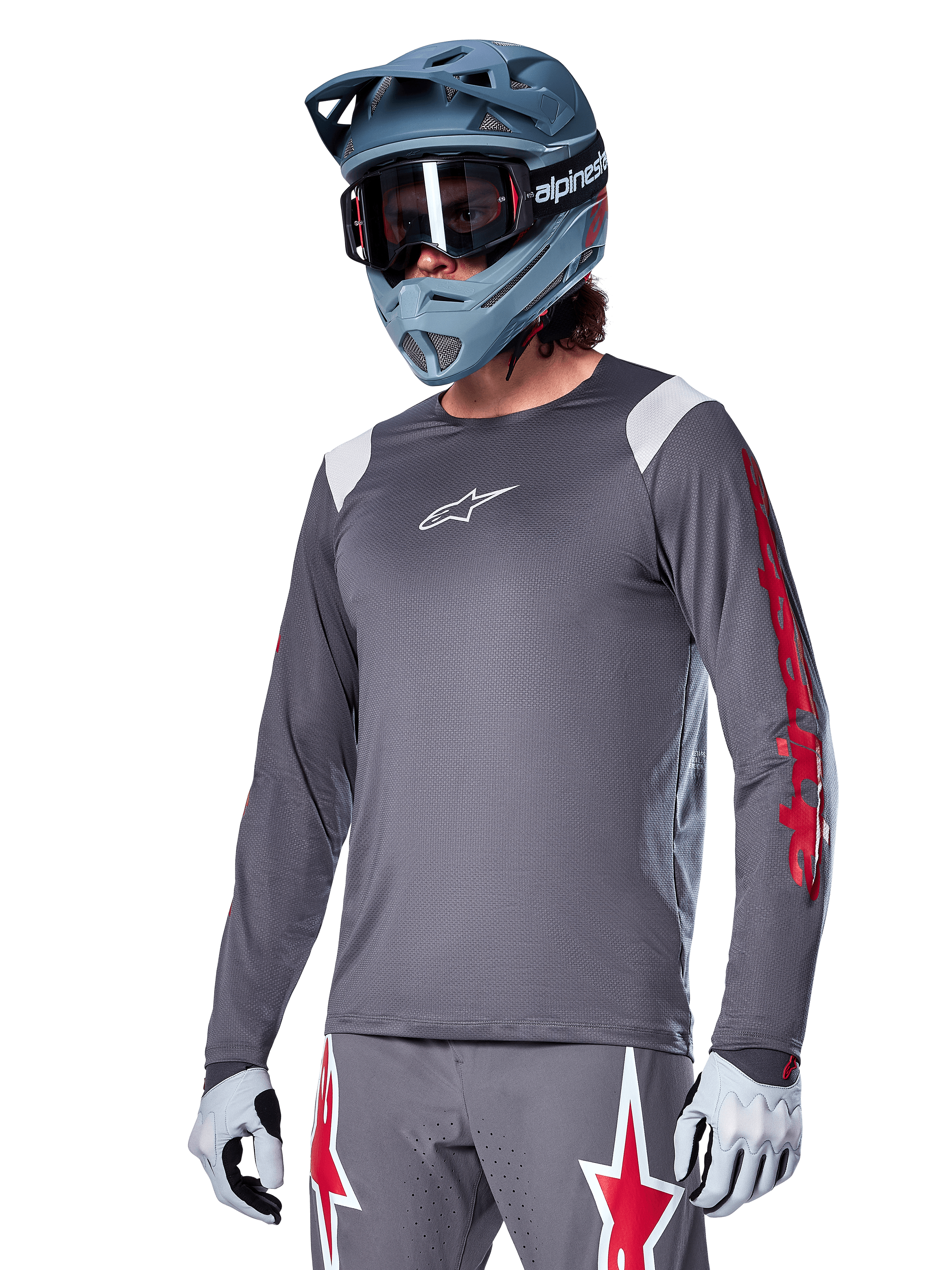 Alpinestars A-Supra Astar Jersey z długim rękawem, koszulka rowerowa MTB, ciemnoszara z czerwonymi i białymi akcentami, sportowy krój, noszona z pasującymi szarymi spodniami z grafiką czerwonych i białych gwiazd, kompletny strój do kolarstwa terenowego z kaskiem full-face i rękawicami
