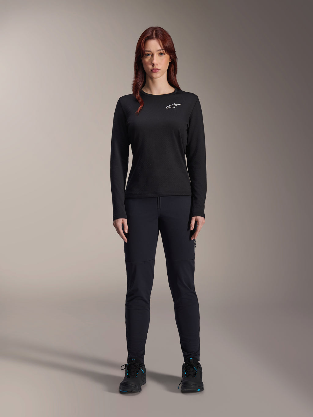 Alpinestars Stella A-Dura Thermal Jersey, damska koszulka rowerowa MTB z długim rękawem, czarna z białym logo na klatce piersiowej, noszona z dopasowanym czarnym strojem i butami rowerowymi, portret studyjny.
