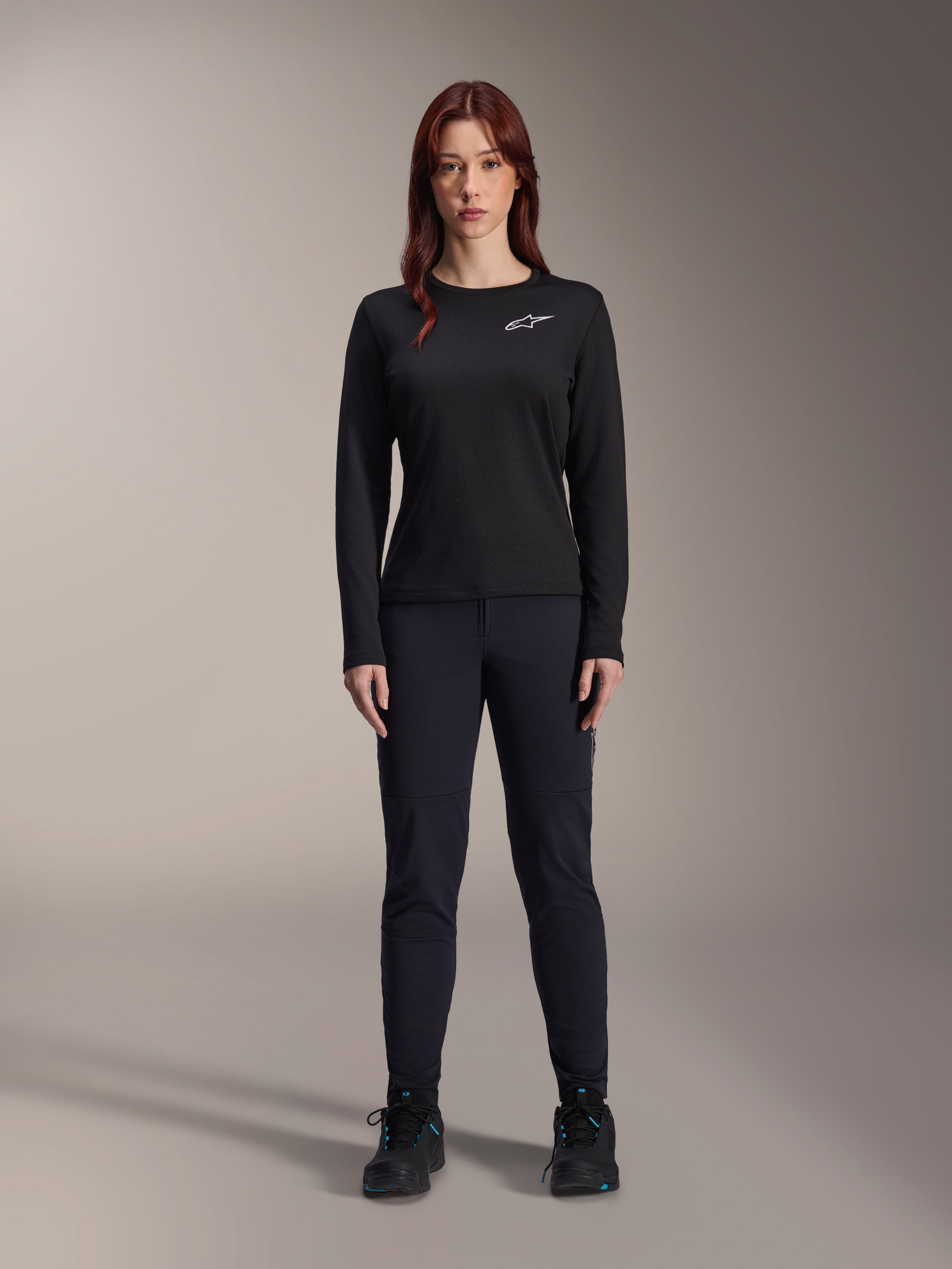 Alpinestars Stella A-Dura Thermal Jersey, damska koszulka rowerowa MTB z długim rękawem, czarna z białym logo na klatce piersiowej, noszona z dopasowanym czarnym strojem i butami rowerowymi, portret studyjny.