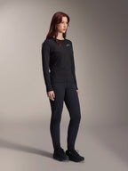 Kobieta ubrana w koszulkę Alpinestars Stella A-Dura Thermal, czarna koszulka MTB z długim rękawem i białym logo na piersi, zestawiona z dopasowanymi czarnymi spodniami i butami sportowymi, portret studyjny profesjonalnej odzieży rowerowej