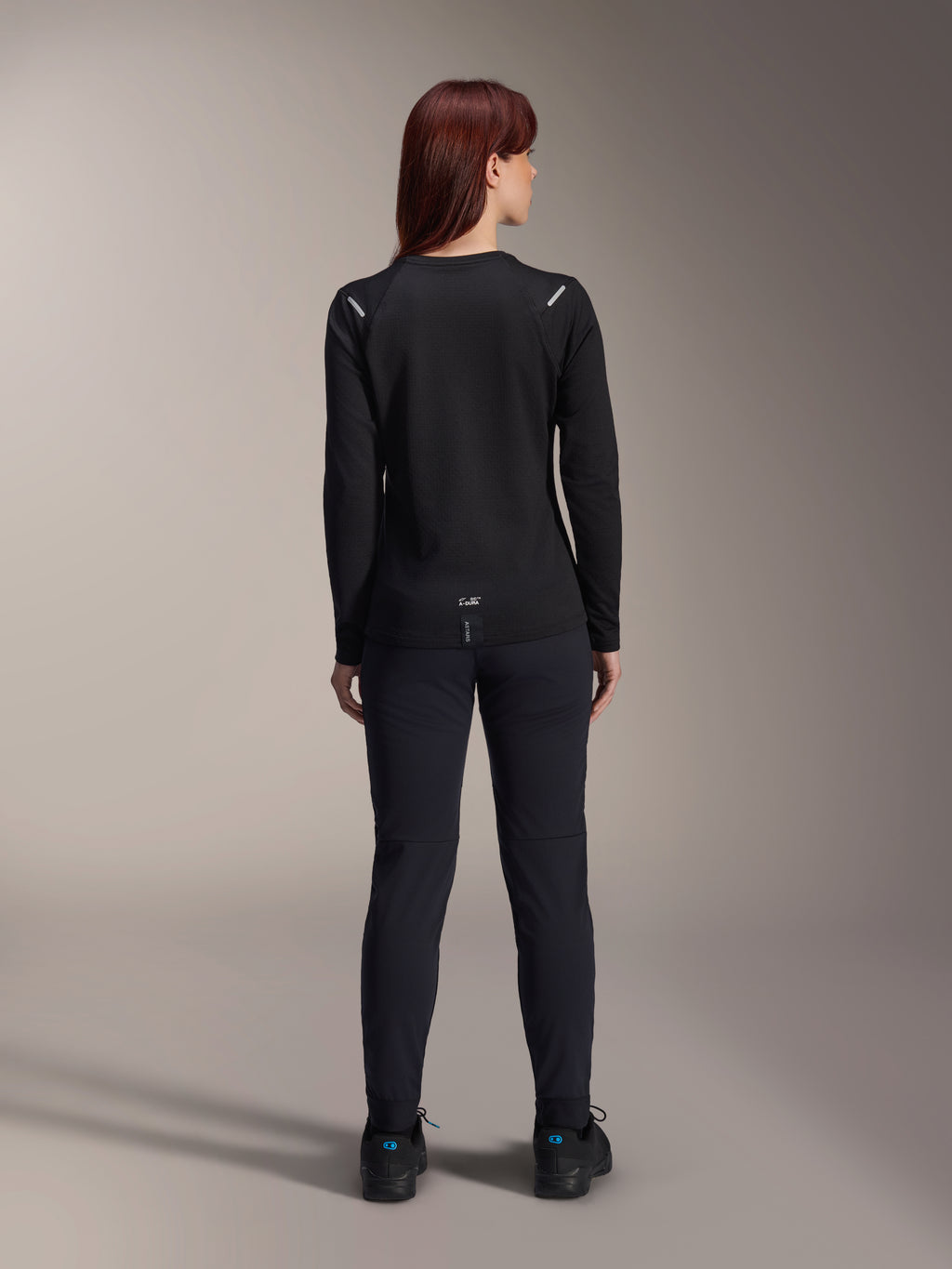 Alpinestars Stella A-Dura Thermal Jersey, damska koszulka rowerowa, widok z tyłu, czarna, ocieplany polar, długi rękaw, zestawiona z czarnymi spodniami i butami, logo A-Dura na dole pleców, odblaskowe detale na ramionach, przeznaczona do jazdy MTB