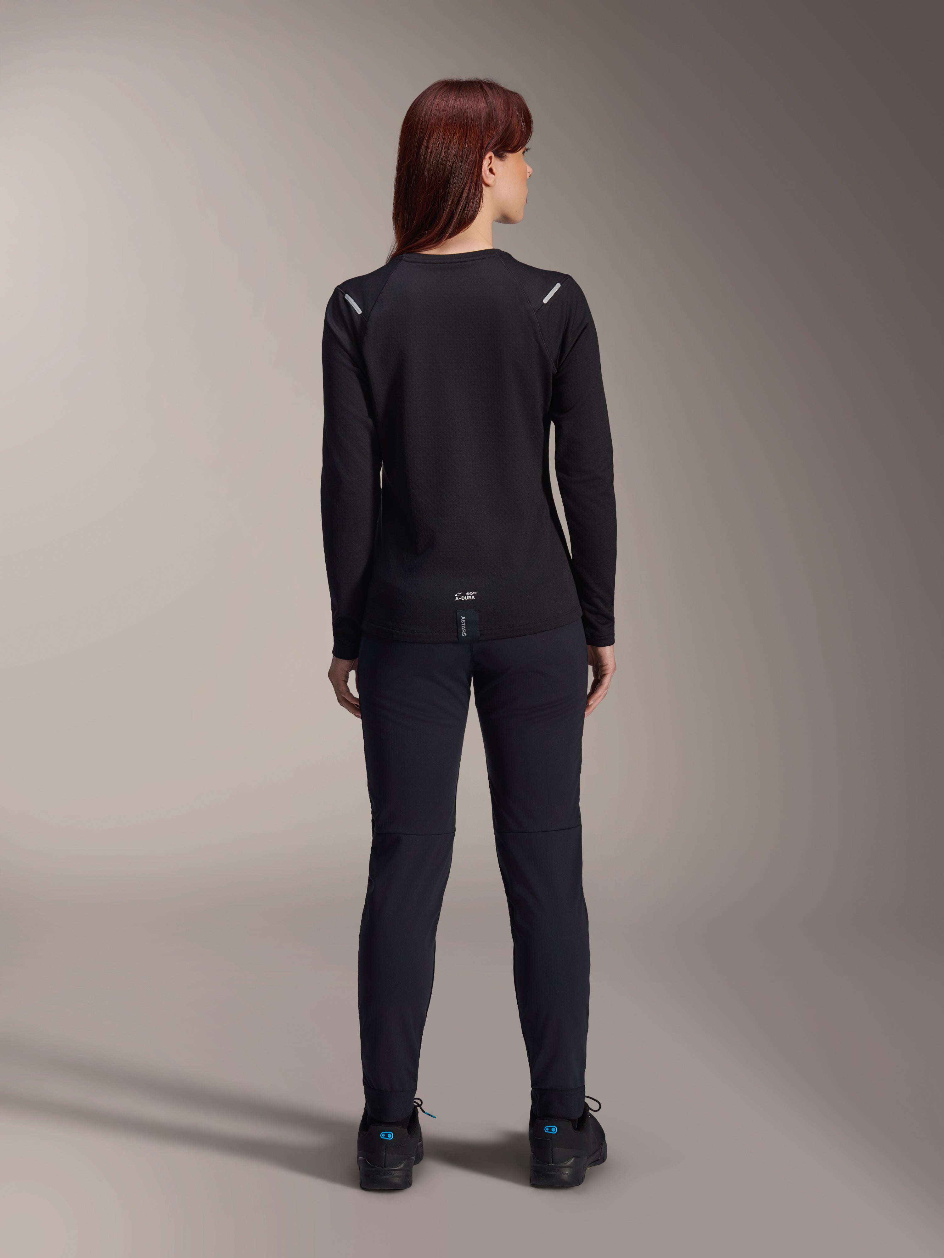 Alpinestars Stella A-Dura Thermal Jersey, damska koszulka rowerowa, widok z tyłu, czarna, ocieplany polar, długi rękaw, zestawiona z czarnymi spodniami i butami, logo A-Dura na dole pleców, odblaskowe detale na ramionach, przeznaczona do jazdy MTB