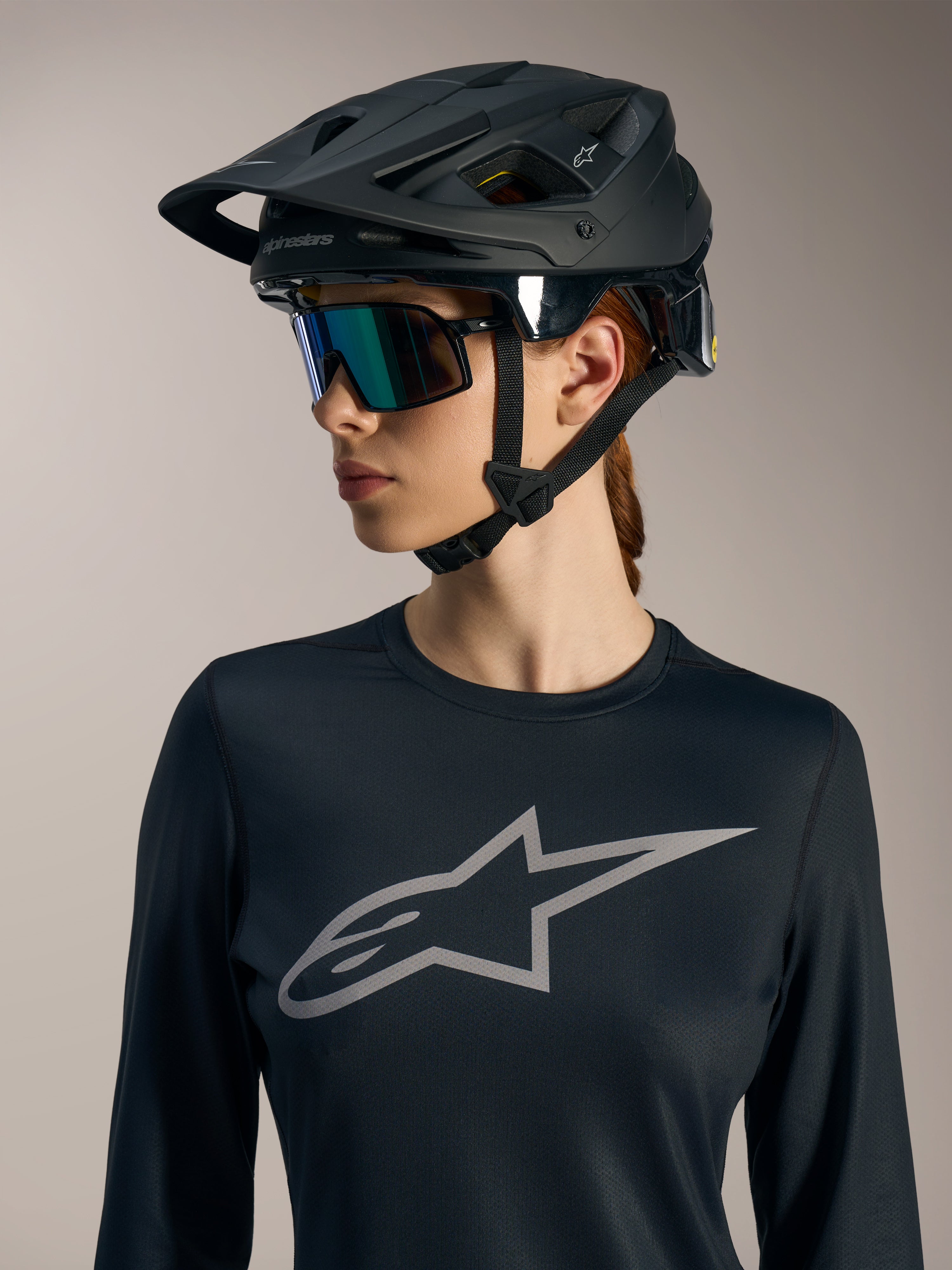 Czarna damska koszulka Stella A-Dura Ride LS z szarym logo Astars, zestawiona z matowym czarnym kaskiem MTB.