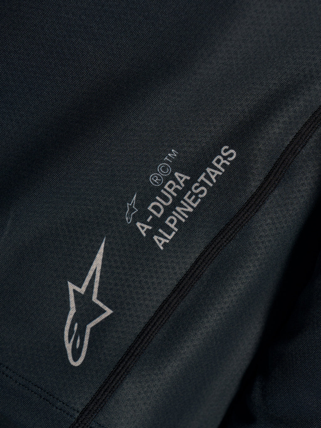 Czarna koszulka Stella A-Dura Ride, zbliżenie na techniczny żakard z logo Astars i napisem A-DURA ALPINESTARS.