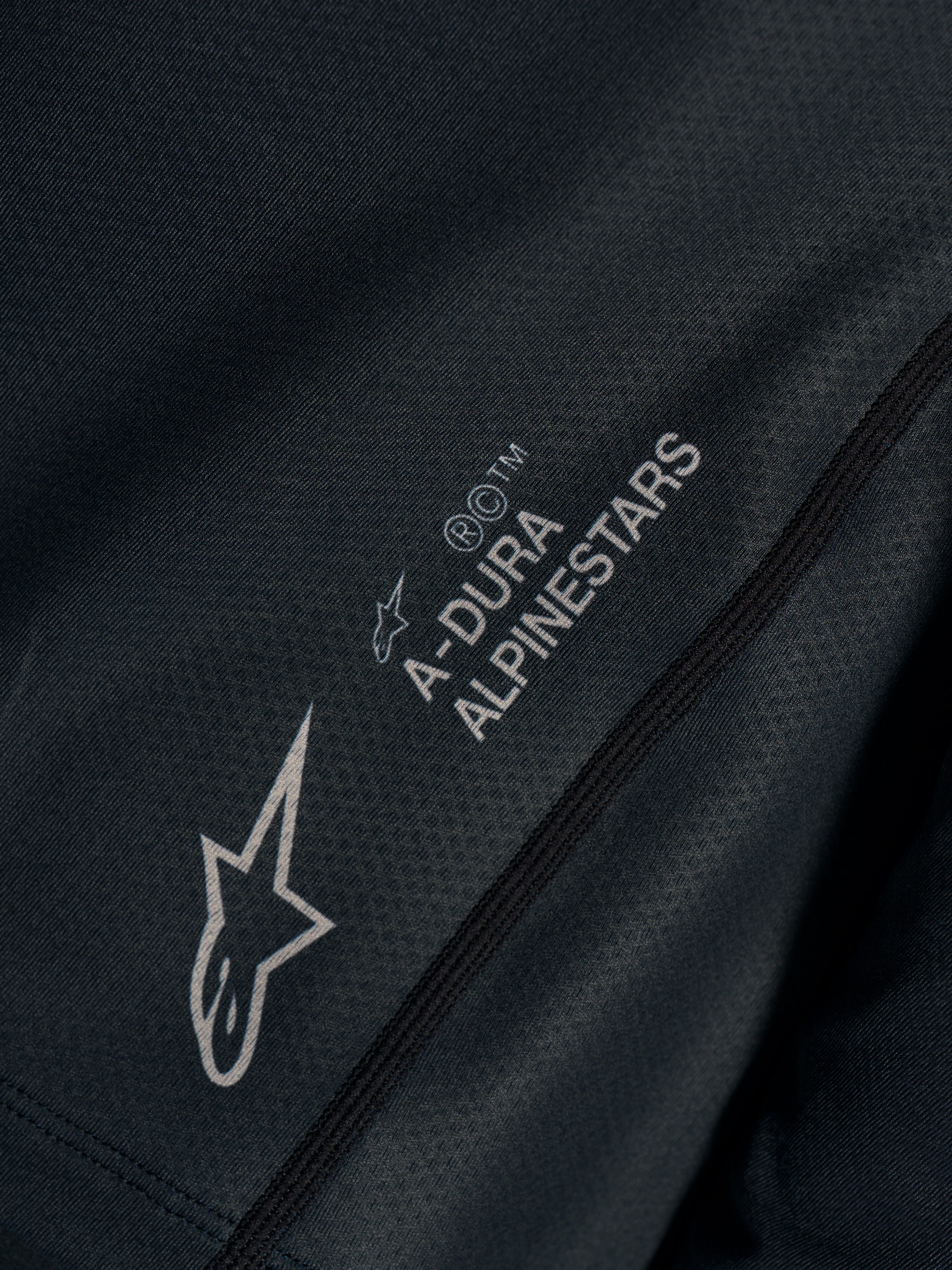 Czarna koszulka Stella A-Dura Ride, zbliżenie na techniczny żakard z logo Astars i napisem A-DURA ALPINESTARS.