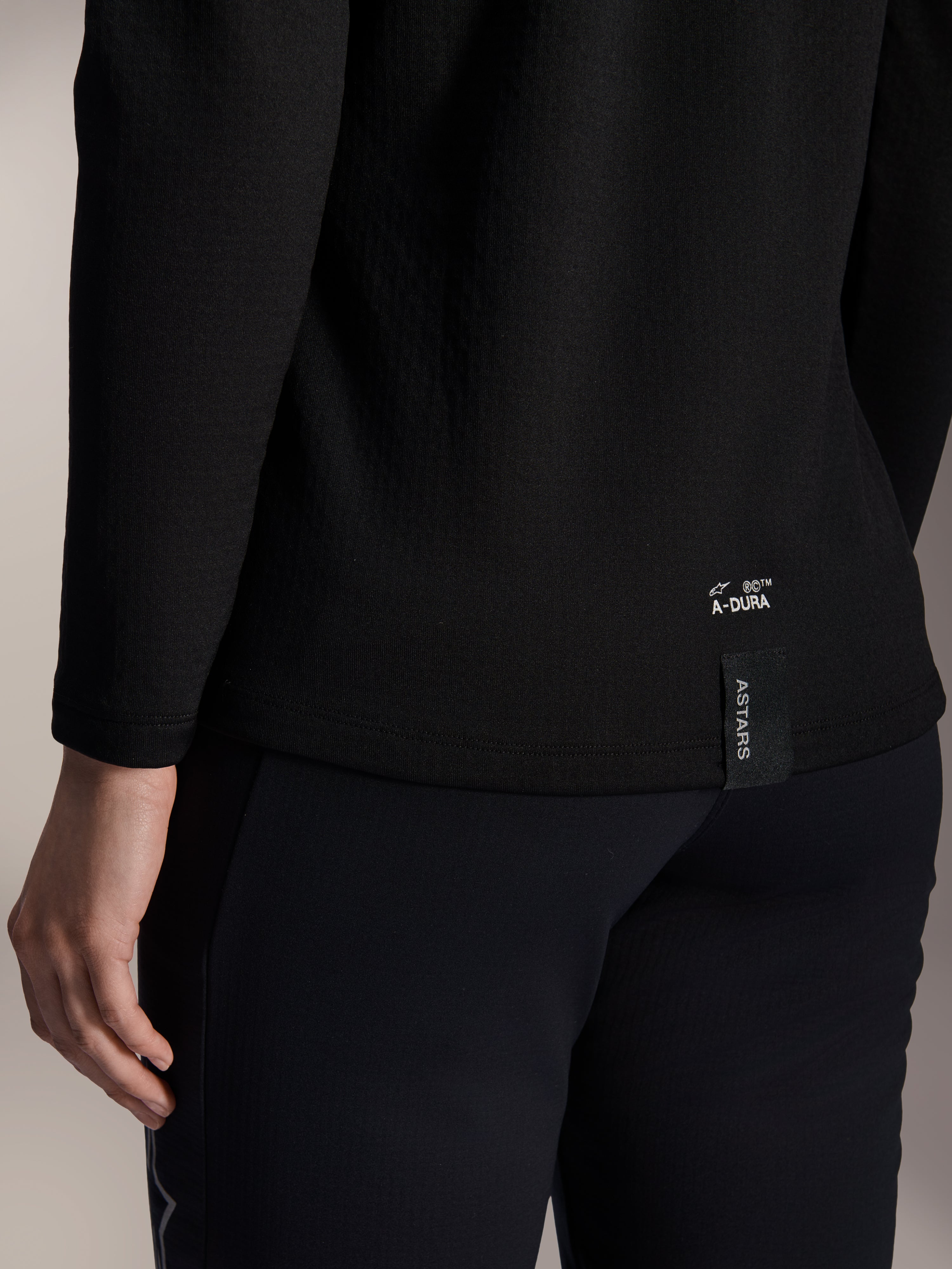 Alpinestars Stella A-Dura Thermal Jersey, czarna damska koszulka termiczna MTB, zbliżenie na dolne wykończenie tyłu z białym brandingiem A-DURA i pionową metką z logo ASTARS, zaprojektowana do jazdy na rowerze górskim w chłodne dni
