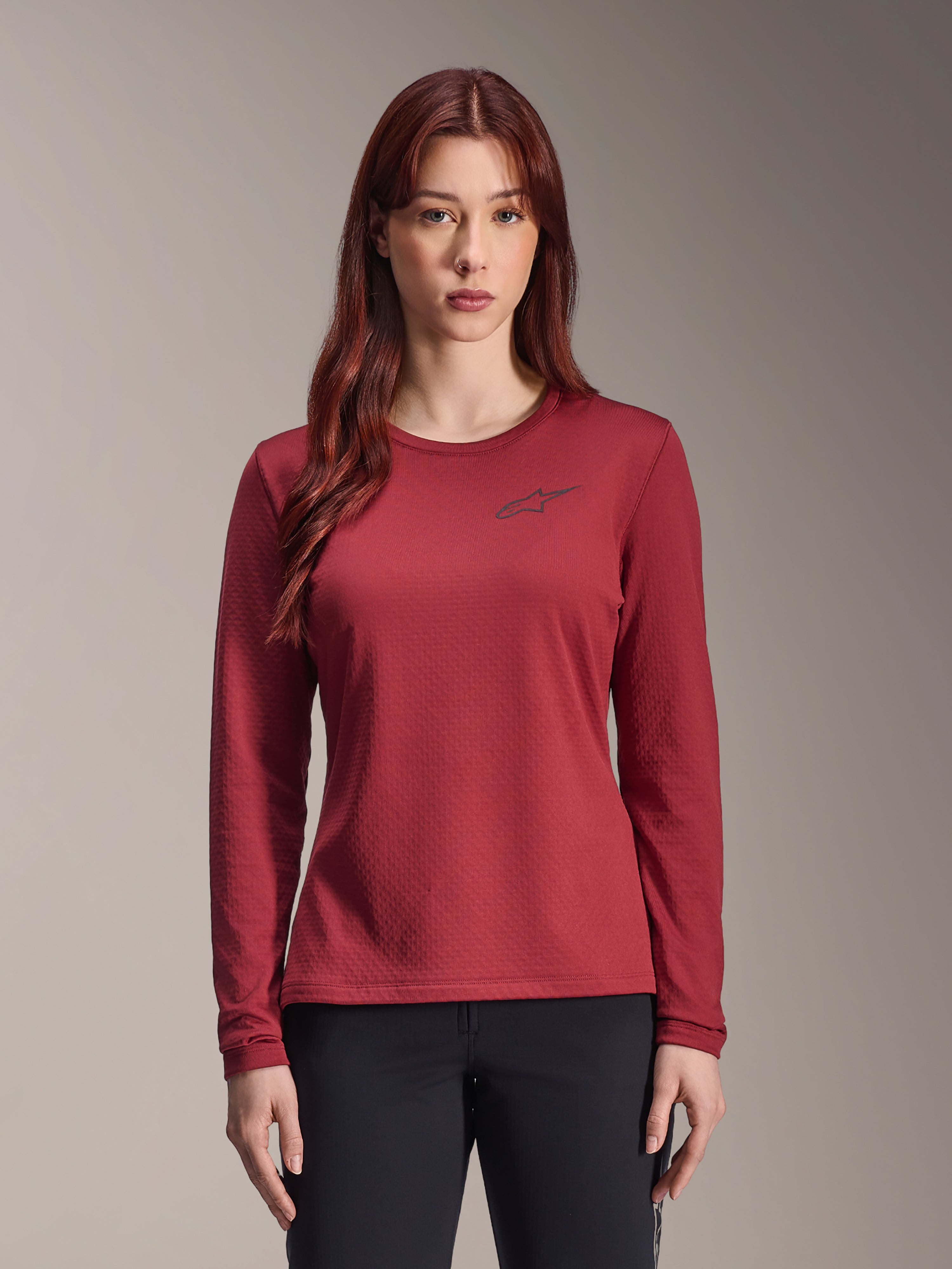 Alpinestars Stella A-Dura Thermal Jersey, damska koszulka MTB z długim rękawem, bordowa, teksturowana tkanina termiczna, okrągły dekolt z małym czarnym logo Alpinestars na piersi, prezentowana przez modelkę.