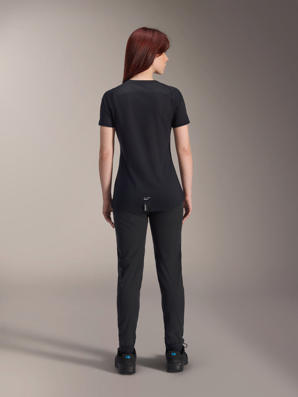 Alpinestars Stella A-Dura Dri Switch Jersey, damska koszulka rowerowa z krótkim rękawem, czarna, widok z tyłu na modelce, przedłużony tył i techniczne panele z siatki, czarne spodnie, wyczynowa odzież MTB