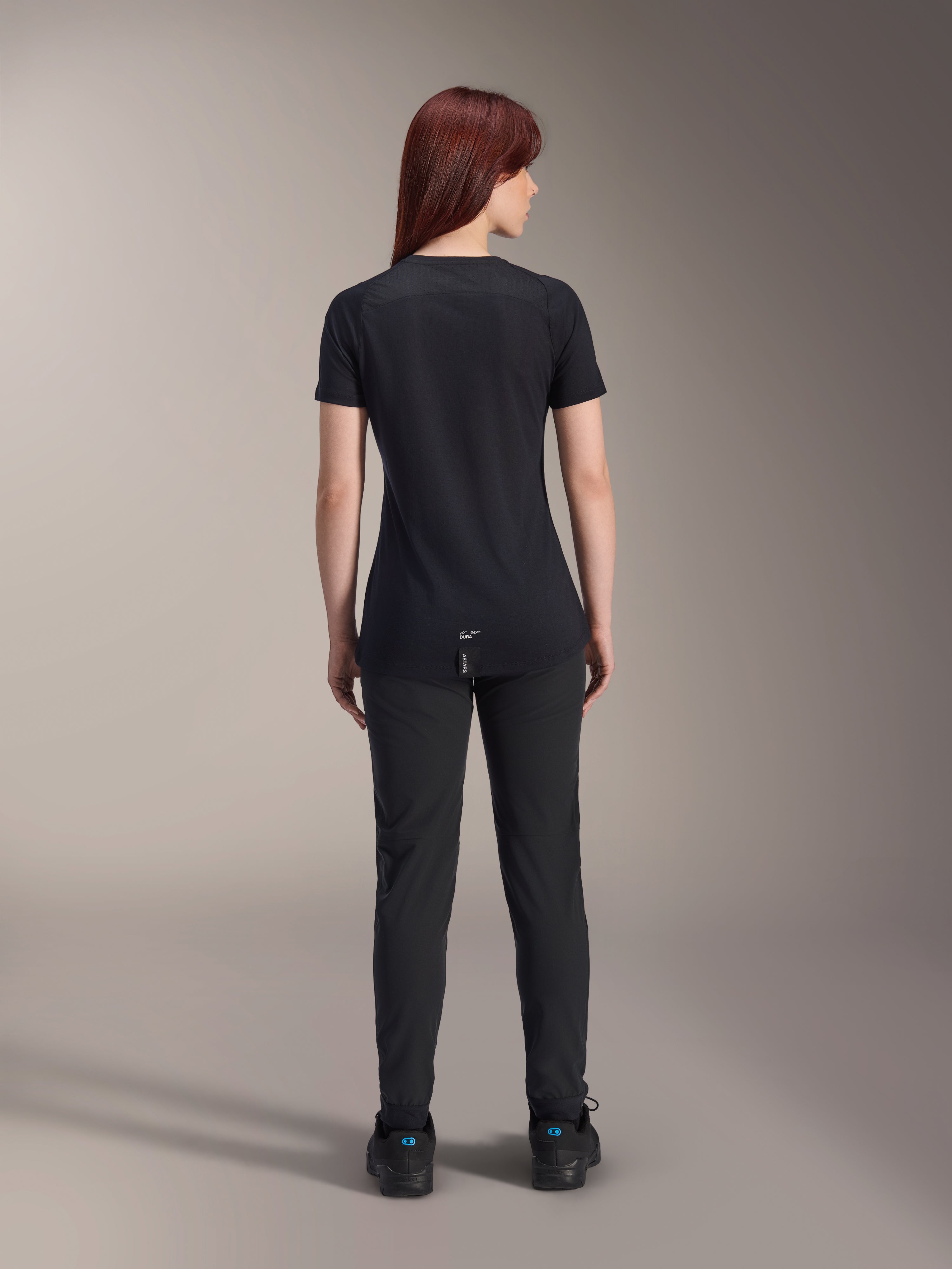 Alpinestars Stella A-Dura Dri Switch Jersey, damska koszulka rowerowa z krótkim rękawem, czarna, widok z tyłu na modelce, przedłużony tył i techniczne panele z siatki, czarne spodnie, wyczynowa odzież MTB