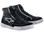 Alpinestars Ageless Riding Shoes, miejskie obuwie motocyklowe, czarne z białymi kontrastowymi szwami i podeszwami, wysoka sylwetka typu sneaker z dużym białym logo gwiazdy z boku, codzienne obuwie ochronne do jazdy szosowej