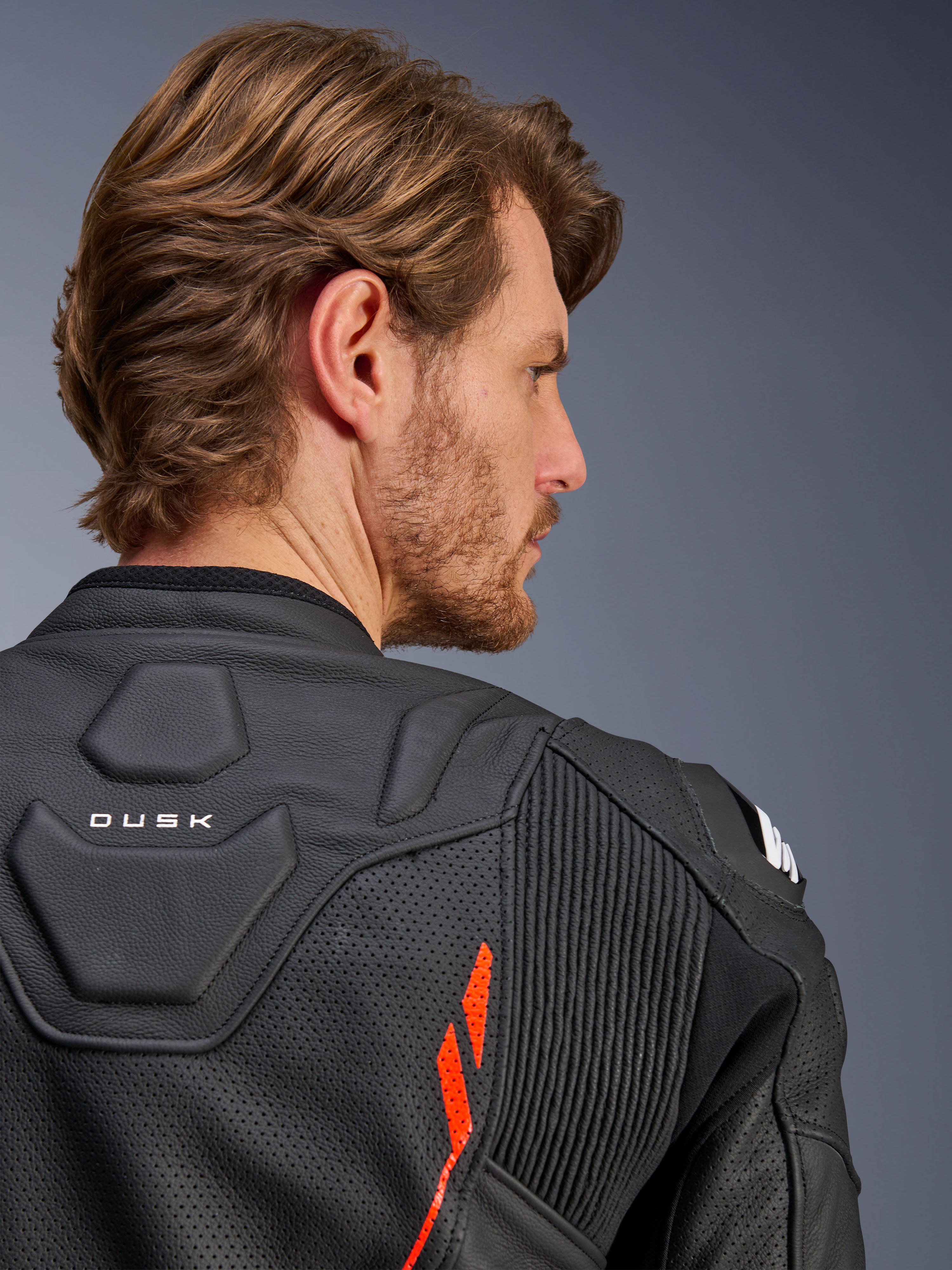 Alpinestars Dusk Airflow Leather Jacket, skórzana kurtka motocyklowa, Black Red Fluo, zbliżenie na górną część pleców i ramię, perforowana skóra zapewniająca wentylację, elastyczne panele akordeonowe, detal z napisem „DUSK”, prezentowana na modelu
