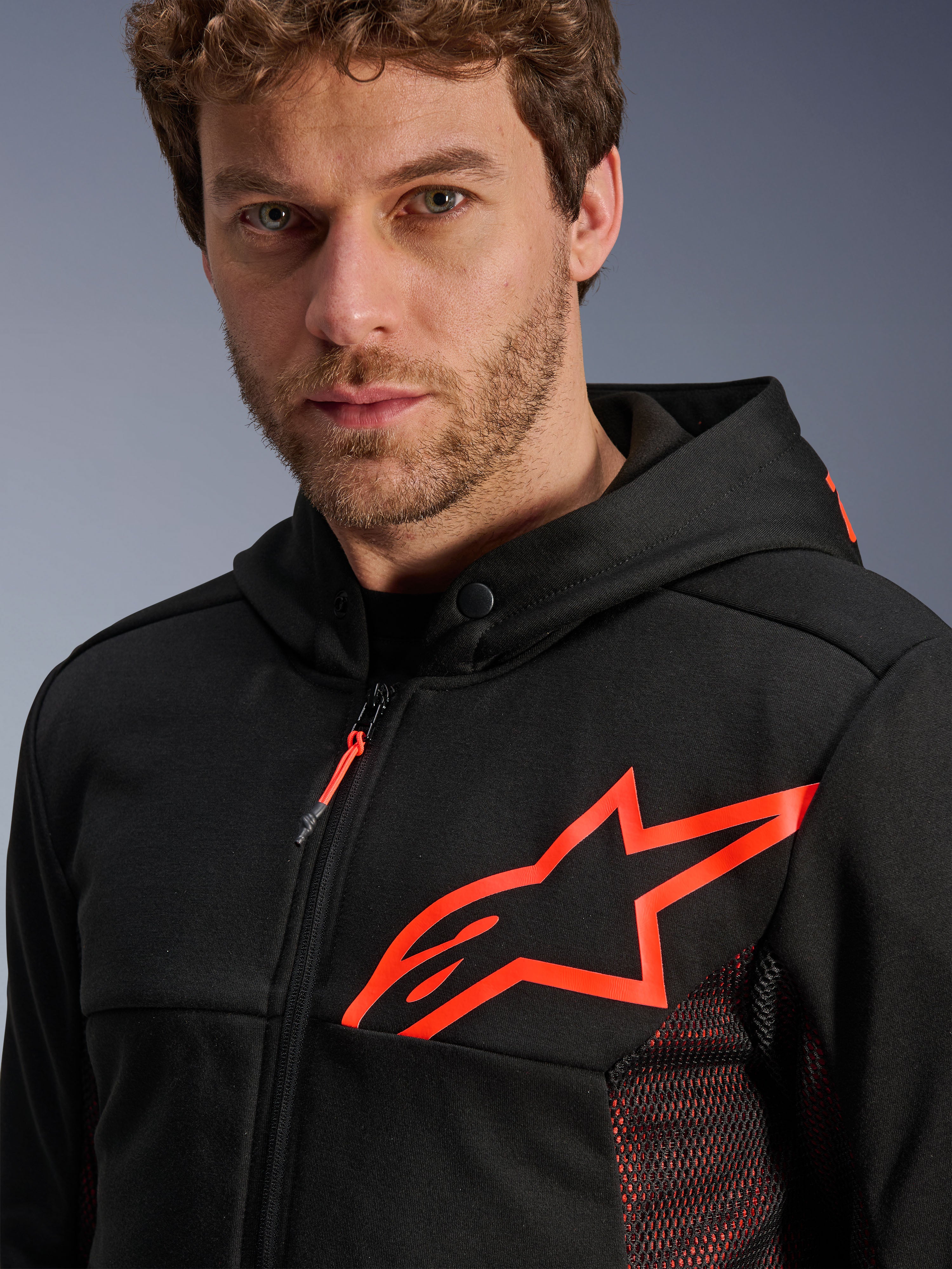 Alpinestars Chrome Air Sport Hoodie, czarno-czerwona (Black and Red Fluo), zbliżenie na duże czerwone fluorescencyjne logo gwiazdy na piersi, czerwone siatkowe panele boczne dla wentylacji, przód zapinany na zamek, kołnierz z zatrzaskiem, miejska odzież motocyklowa