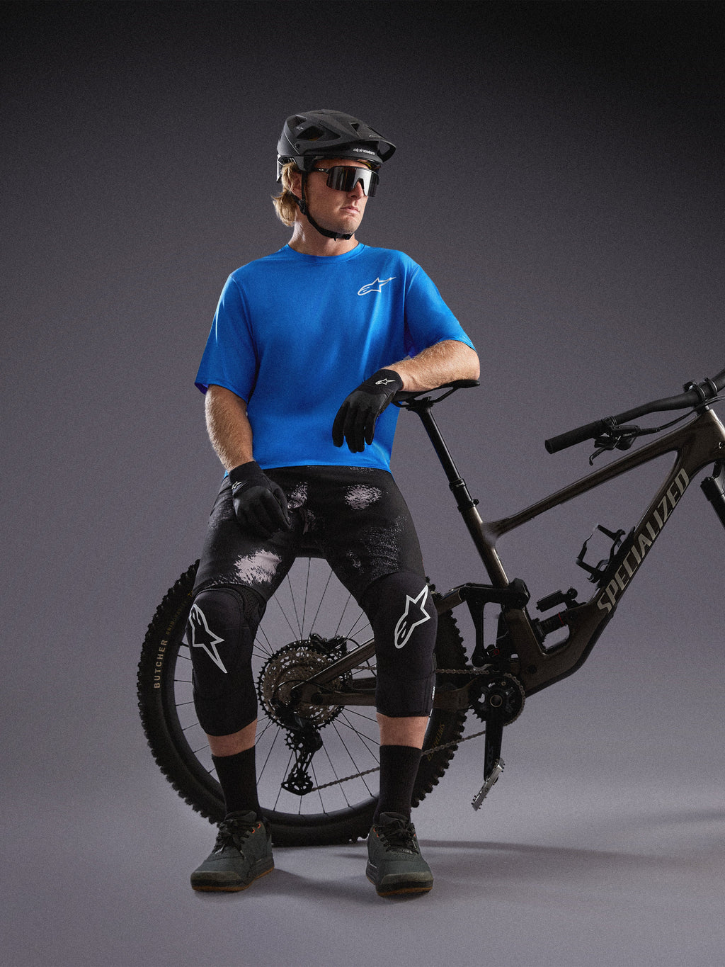Kolarz w niebieskiej koszulce Alpinestars A-Dura Air SS i szortach Black Camo Ride przy rowerze górskim.