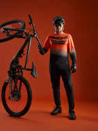 Koszulka A-Dura ASTARS 2.0 z długim rękawem, pomarańczowo-czarny gradient, logo na piersi i pełny sprzęt MTB.