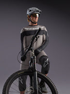 Szara koszulka Alpinestars A-Dura Race LS na rowerzyście MTB, czarne akcenty, profesjonalny sprzęt kolarski.