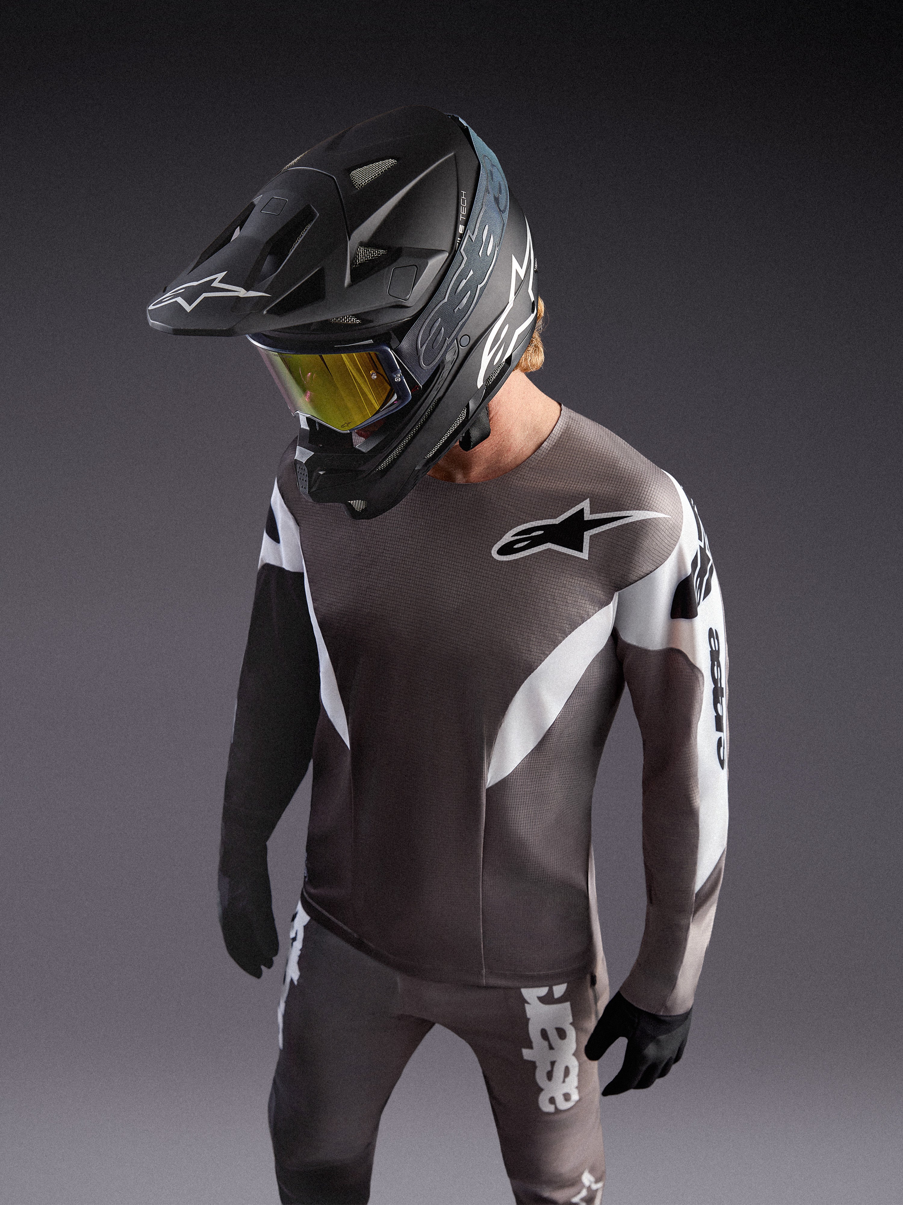 Alpinestars A-Supra Elite Koszulka Faded Gray, szara koszulka MTB z logo ASTARS, zawodnik w czarnym kasku i goglach.