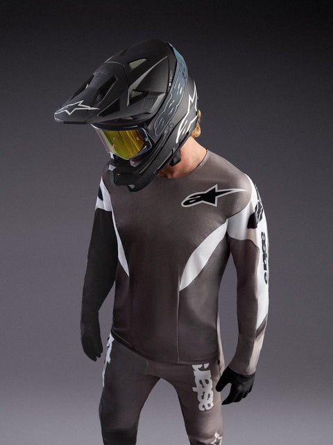 Alpinestars A-Supra Elite Koszulka Faded Gray, szara koszulka MTB z logo ASTARS, zawodnik w czarnym kasku i goglach.
