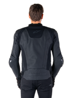 Rear view of a rider wearing the Alpinestars Missile V3 Leather Jacket in black, featuring premium leather construction with technical stretch panels, embossed Alpinestars logo on the lower back, and subtle branding on the upper back, paired with black pants for a coordinated racing sport look.
