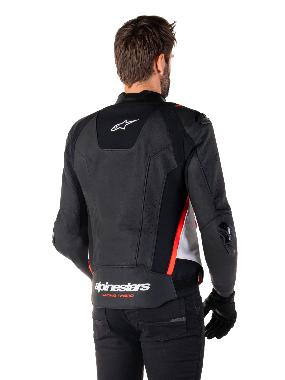Skórzana kurtka Alpinestars Missile V3, widok z tyłu na motocykliście, kolor czarno-biały z czerwonymi akcentami fluo, z wyraźnym brandingiem Alpinestars i napisem „RACING AHEAD” w dolnej części pleców, wykonana z najwyższej jakości skóry z technicznymi panelami elastycznymi i ochronnymi sliderami TPU, zestawiona z czarnymi rękawicami i spodniami.
