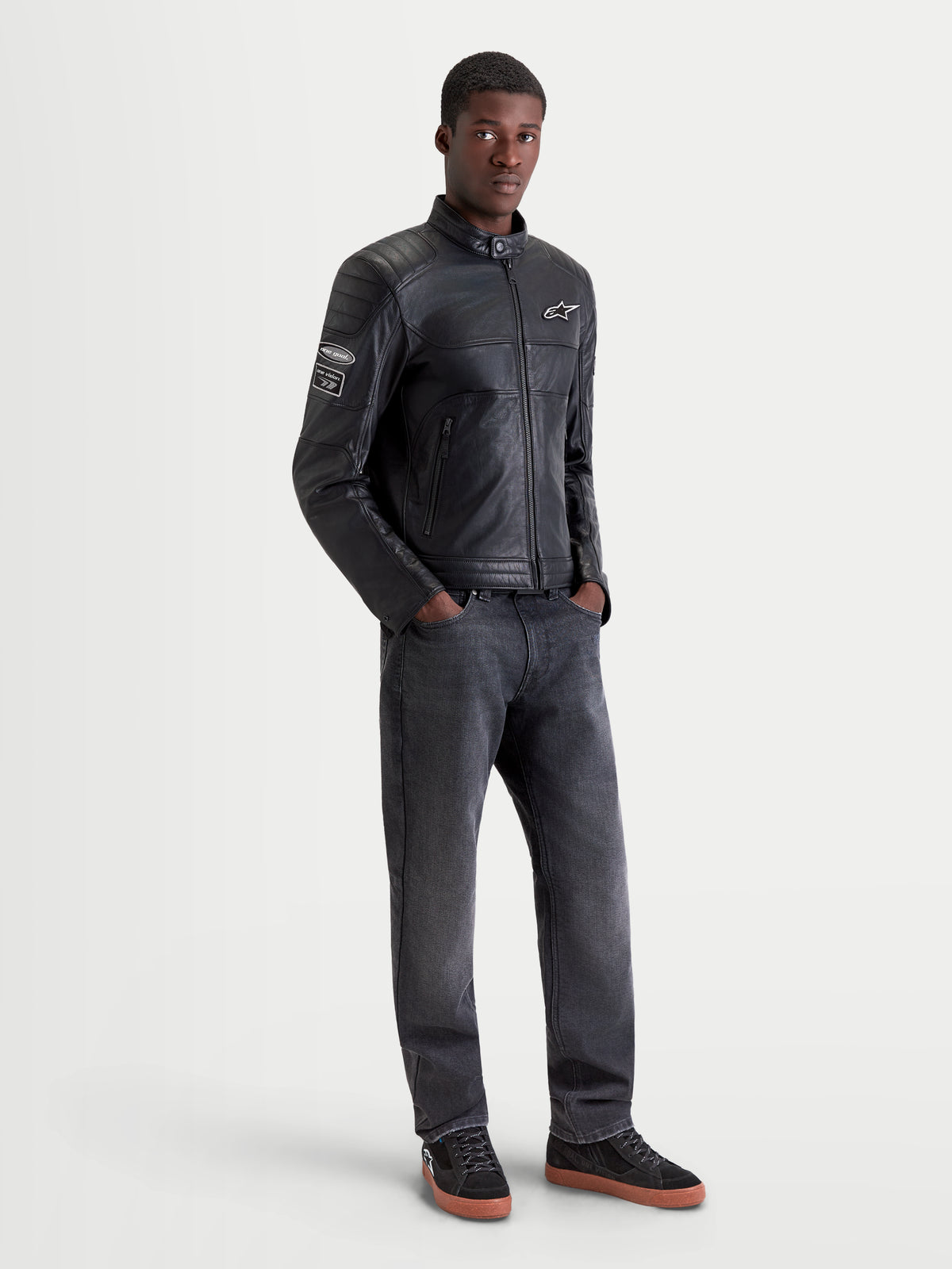 Alpinestars Revern Kurtka skórzana, męska urbanistyczna motocyklowa kurtka skórzana, czarna, widok z przodu na modela ubranego w ciemne jeansy i buty motocyklowe, z detalami w stylu heritage oraz konstrukcją z postarzanej skóry licowej