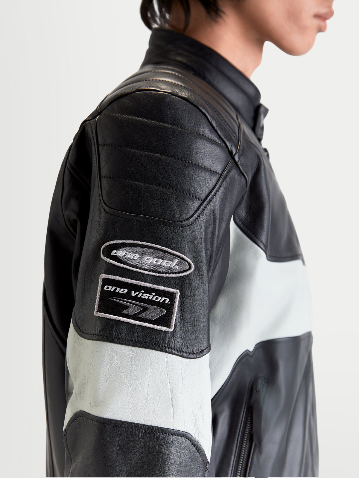 Alpinestars Revern Kurtka skórzana męska miejska motocyklowa w kolorze czarnym i szarym metalicznym, zbliżenie profilu bocznego przedstawiające naszywki z motywem dziedzictwa na rękawie i konstrukcję z postarzanej skóry bydlęcej noszoną przez modela