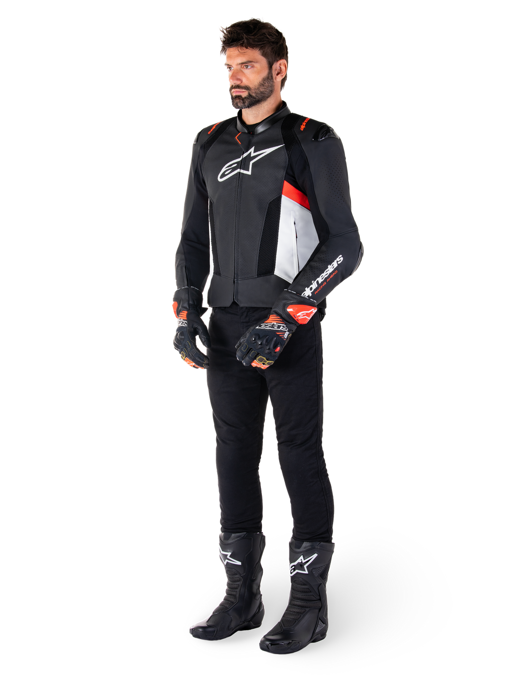 Skórzana kurtka Alpinestars Missile V3 Airflow, Black White Red Fluo, noszona przez modela w czarnych spodniach, czarnych rękawicach wyścigowych i czarnych butach, z perforowaną skórą dla wentylacji, białym logo na klatce piersiowej i czerwonymi akcentami fluo, zaprojektowana dla najwyższej wydajności wyścigowej i sportowej.