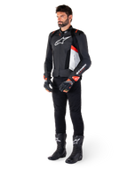 Skórzana kurtka Alpinestars Missile V3 Airflow, Black White Red Fluo, noszona przez modela w czarnych spodniach, czarnych rękawicach wyścigowych i czarnych butach, z perforowaną skórą dla wentylacji, białym logo na klatce piersiowej i czerwonymi akcentami fluo, zaprojektowana dla najwyższej wydajności wyścigowej i sportowej.