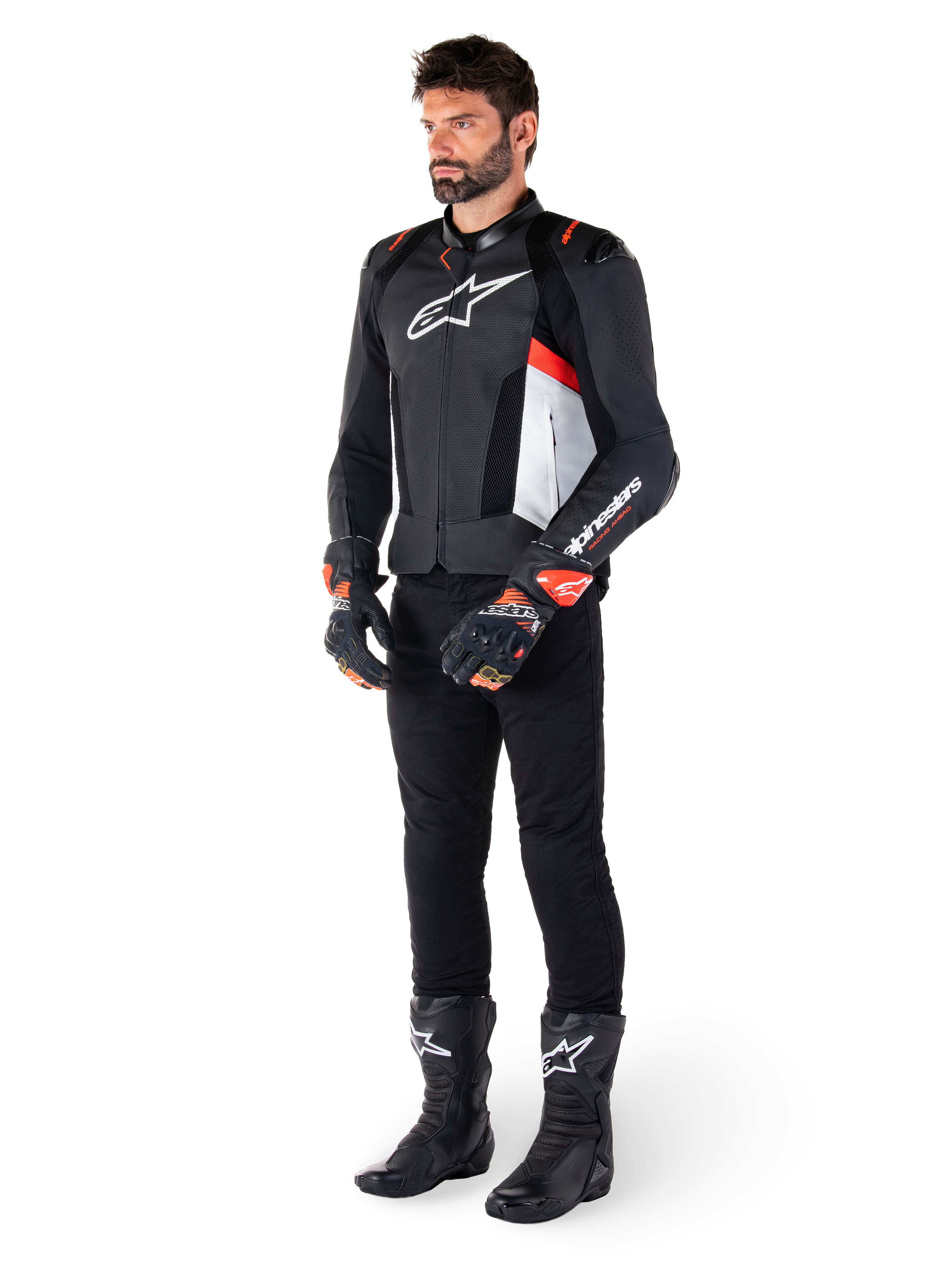 Skórzana kurtka Alpinestars Missile V3 Airflow, Black White Red Fluo, noszona przez modela w czarnych spodniach, czarnych rękawicach wyścigowych i czarnych butach, z perforowaną skórą dla wentylacji, białym logo na klatce piersiowej i czerwonymi akcentami fluo, zaprojektowana dla najwyższej wydajności wyścigowej i sportowej.